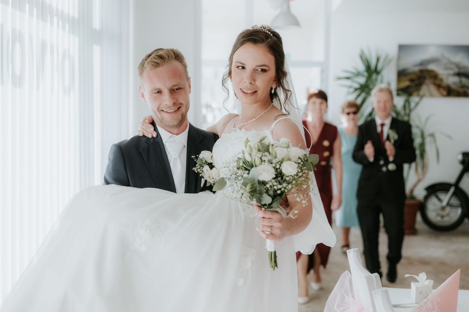 Bride holding white bouquet with groom in suit at elegant indoor wedding ceremony.