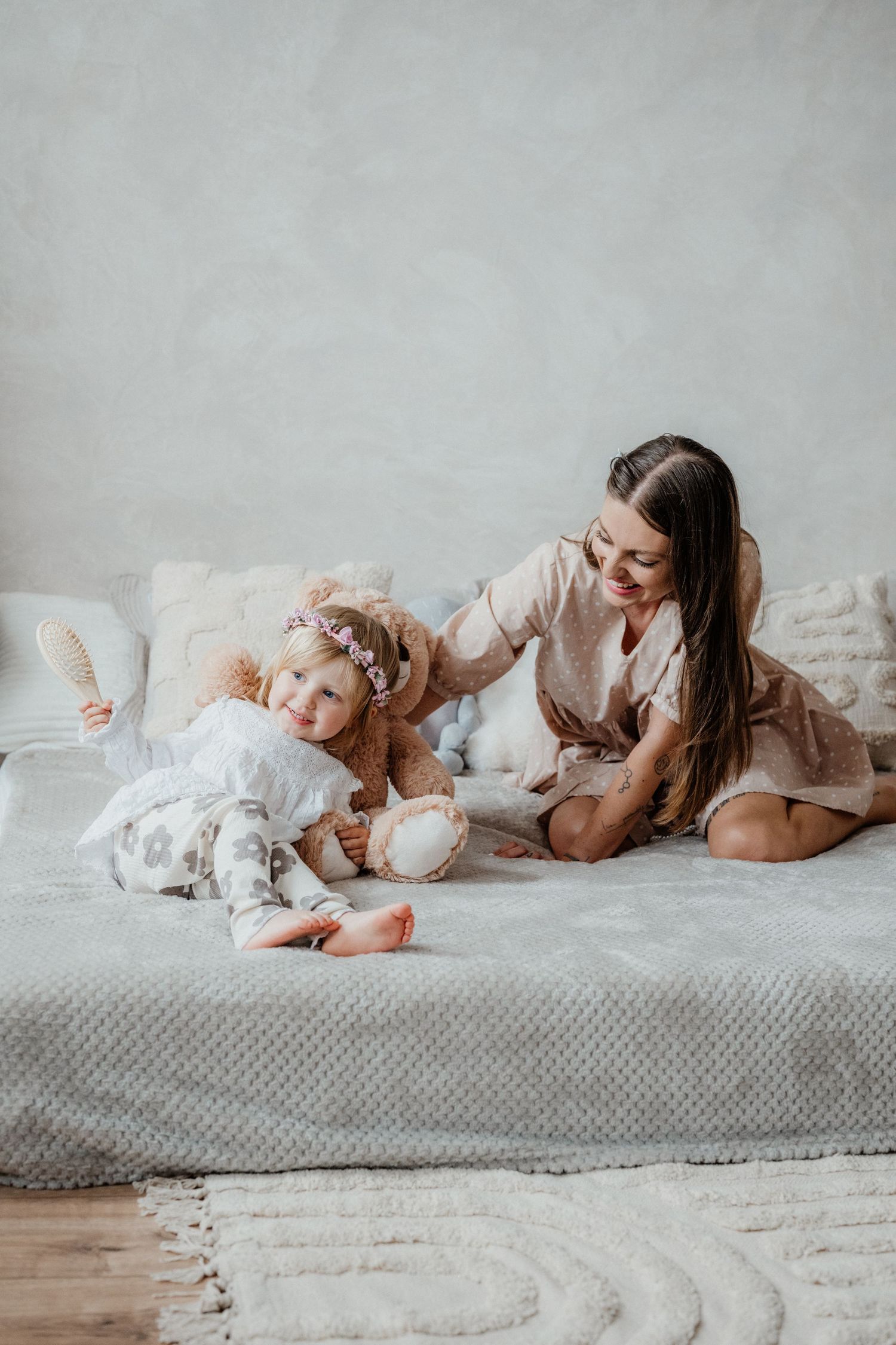 Mother and toddler daughter playing together on a bed with stuffed animals.