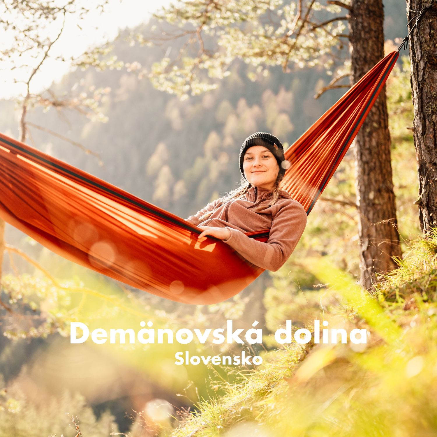 Smiling person relaxing in an orange hammock among trees in Demanovska dolina, Slovakia.