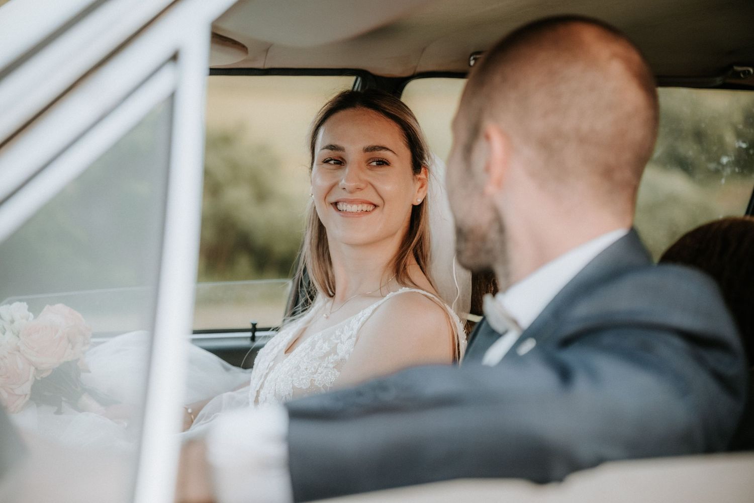 Bride smiling at groom while sitting together in a vintage car on their wedding day.