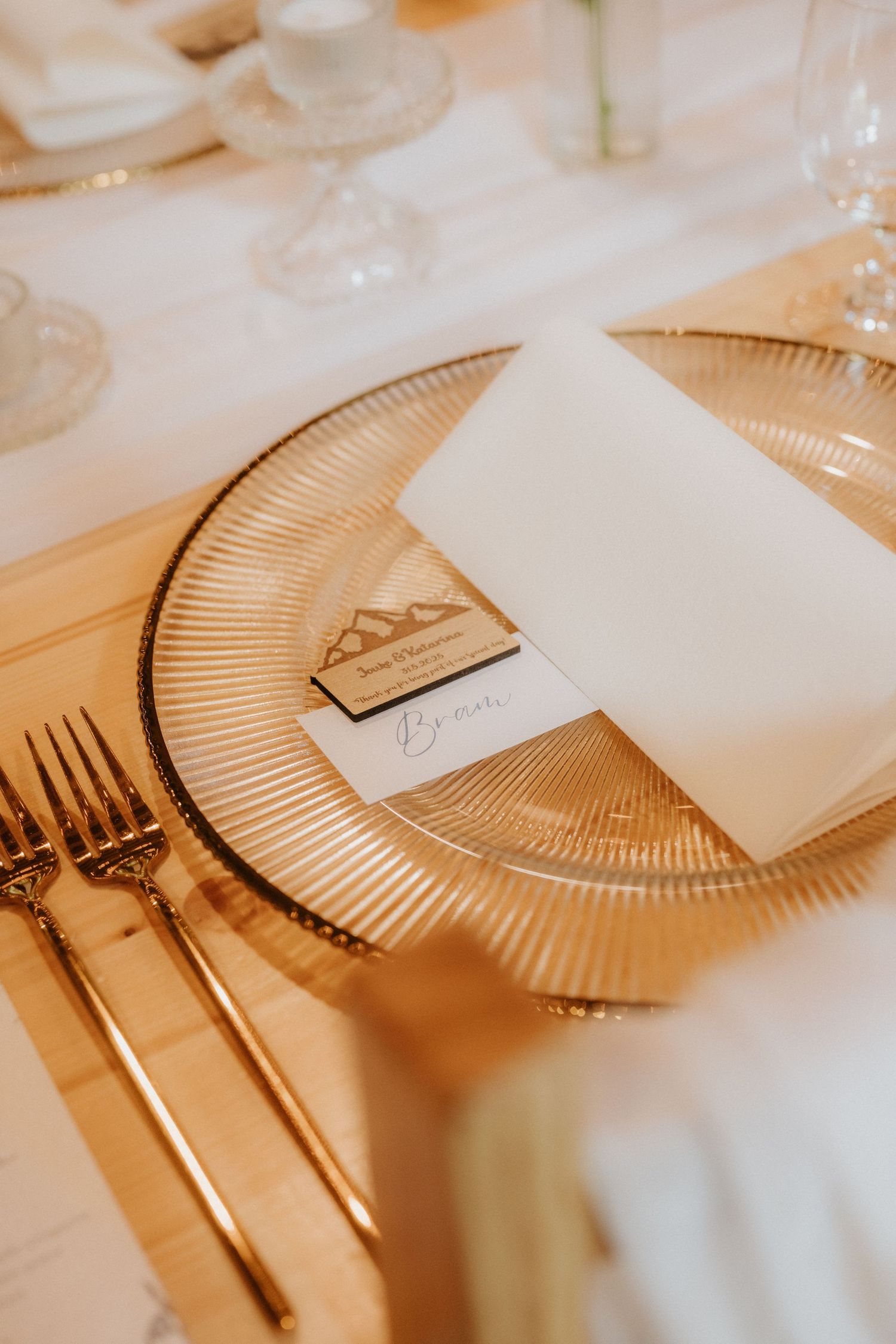 Elegant gold charger plate with white napkin, place card, and gold cutlery on a white tablecloth at a wedding reception.
