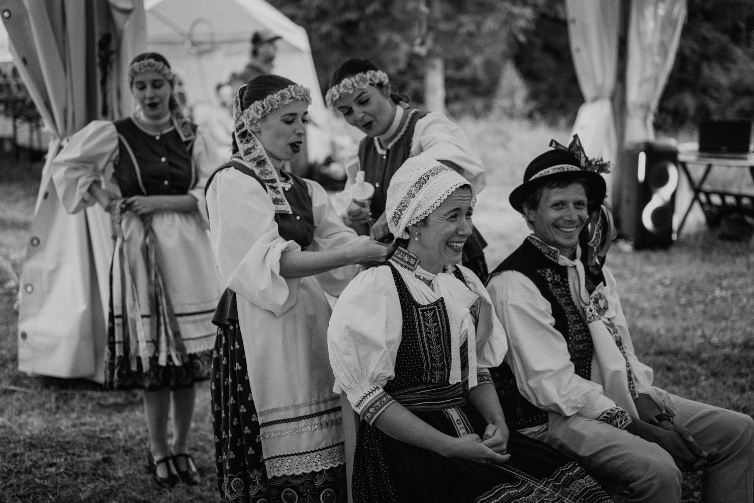 Black and white photo of people in traditional folk costumes smiling at an outdoor cultural festival.