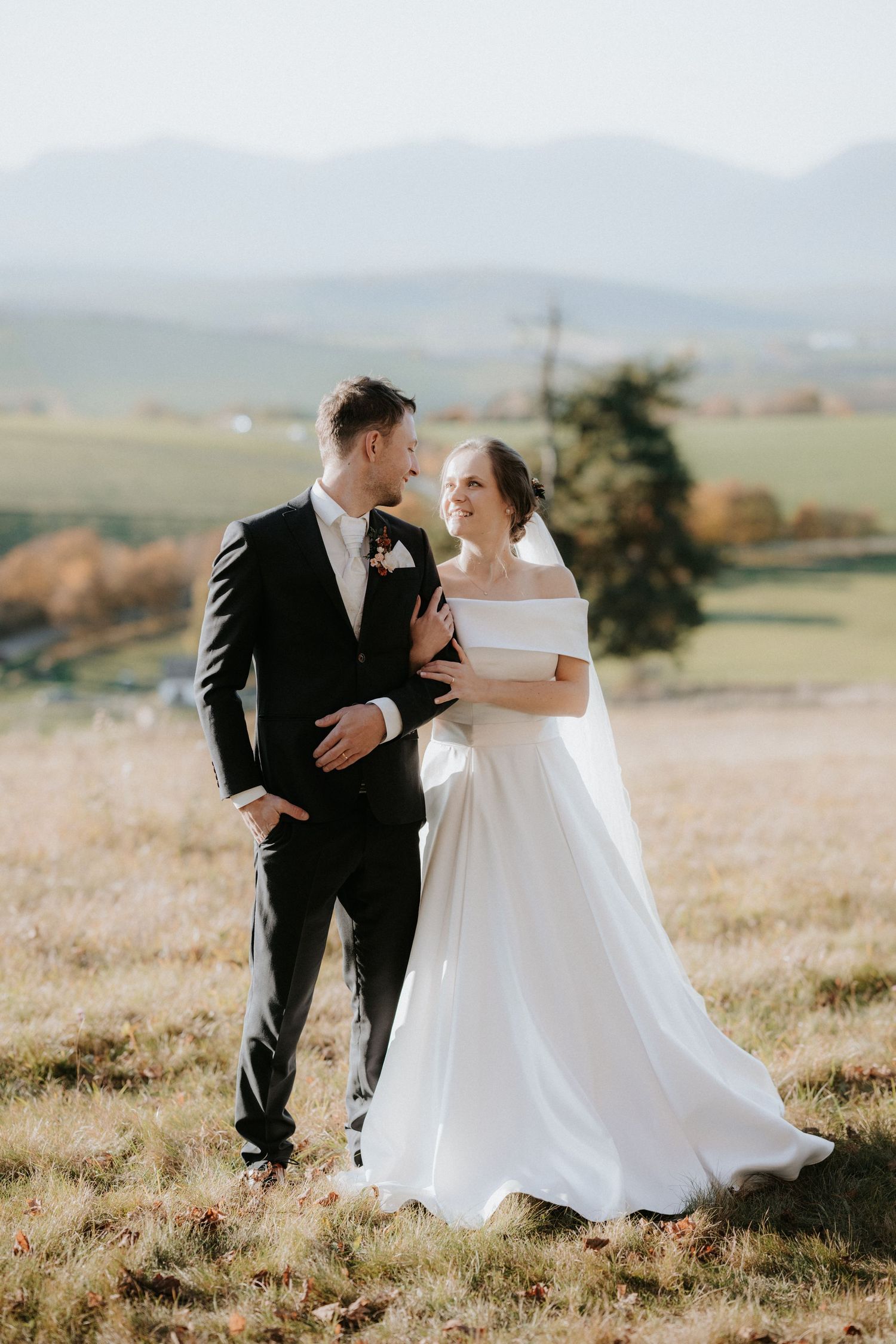 A bride and groom share a romantic moment outdoors with scenic mountain views and green fields in the background.