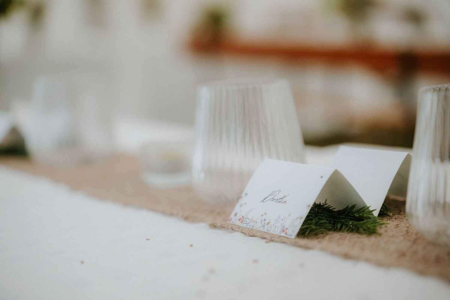 Elegant white place card on burlap table runner with ribbed glass and moss wedding table decor.