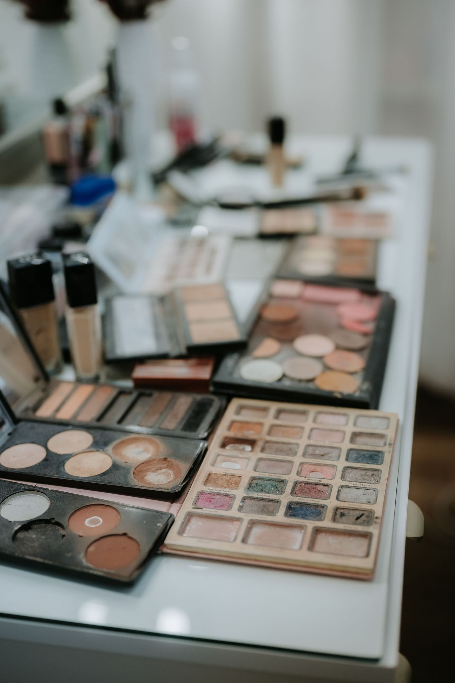 Assorted makeup palettes, eyeshadows, and cosmetics arranged on a white vanity table in a beauty studio.