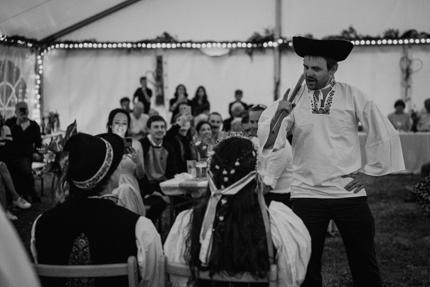 Black and white photo of performers in traditional folk costumes entertaining guests at an outdoor wedding reception.