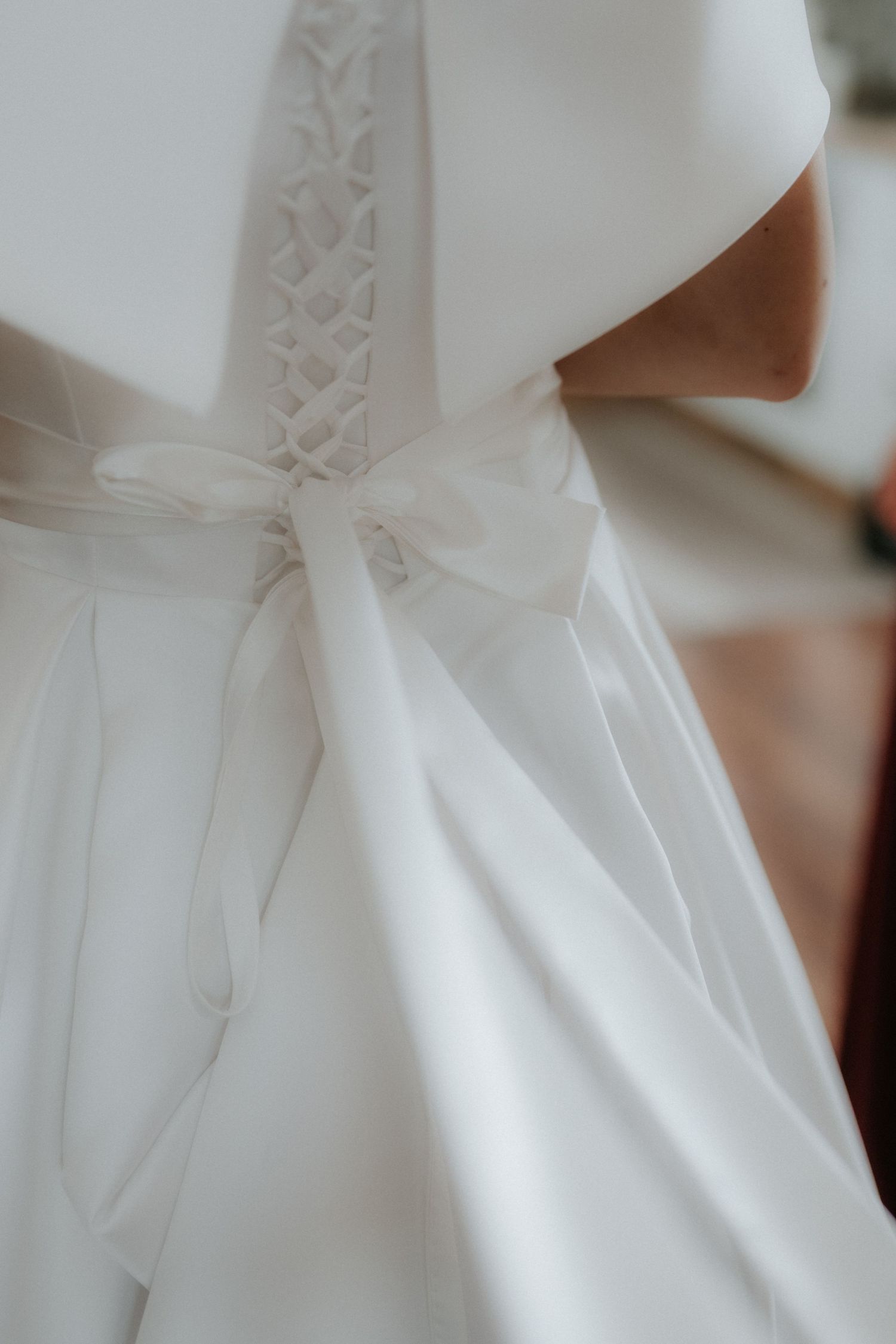Close-up of an elegant white wedding dress back with delicate lace corset detailing and a satin ribbon bow.