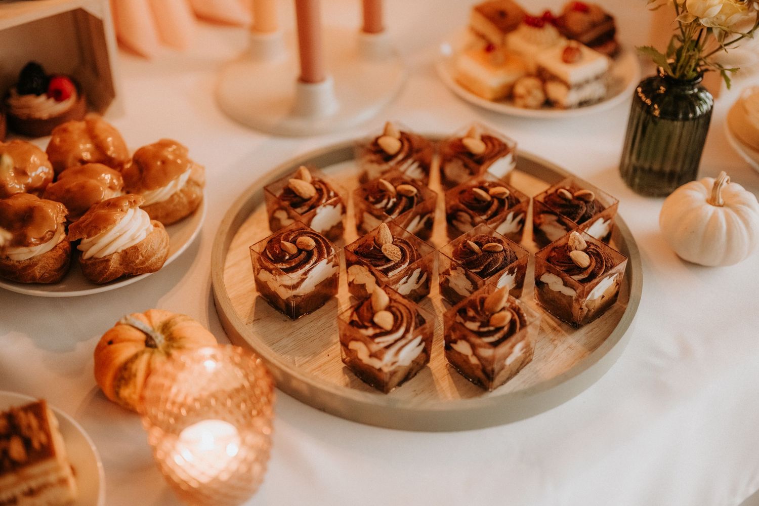 Elegant dessert table with caramel pastries on wooden board, mini donuts, and white pumpkins for fall wedding.