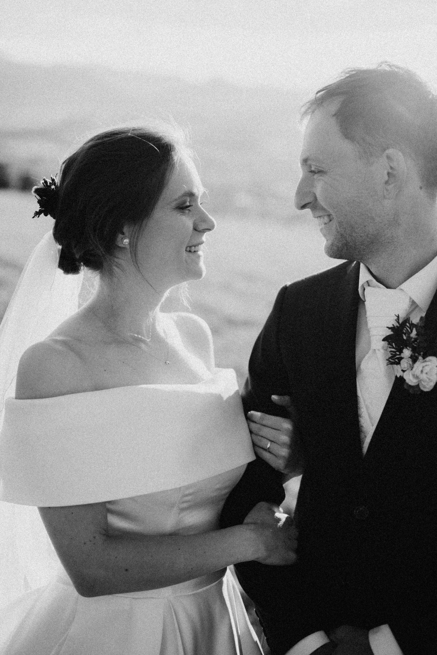 Black and white photo of a smiling bride and groom gazing at each other on their wedding day.