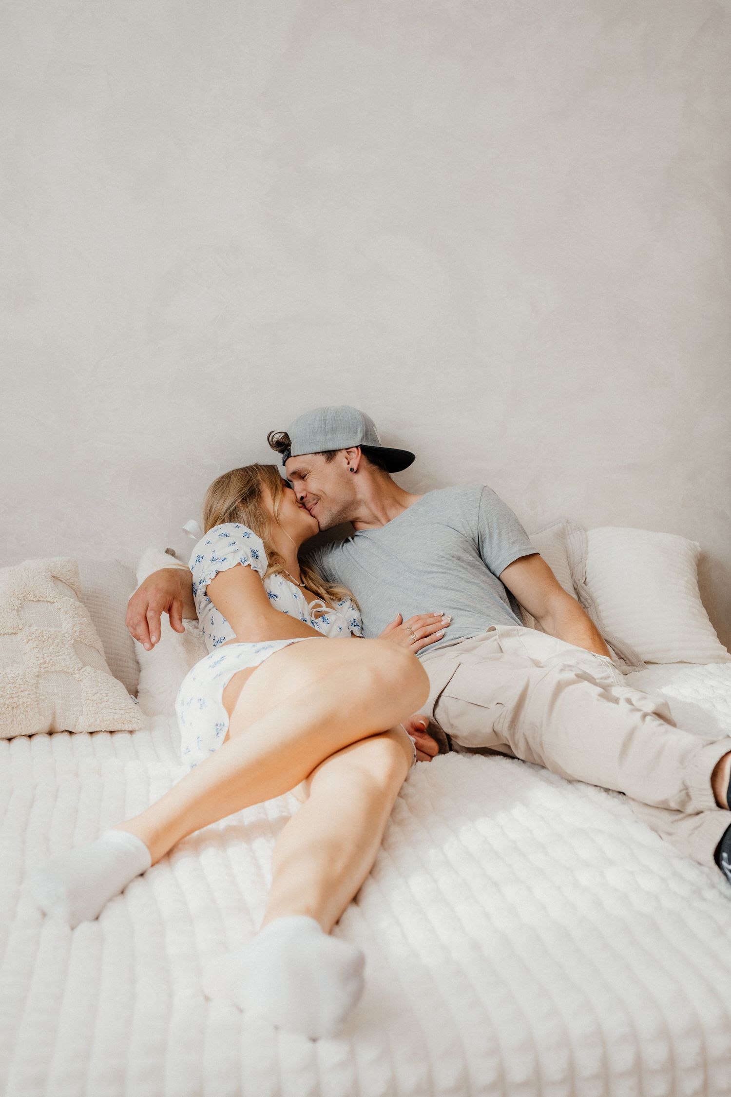 Romantic couple sharing a kiss while lying together on a white bed with soft pillows.