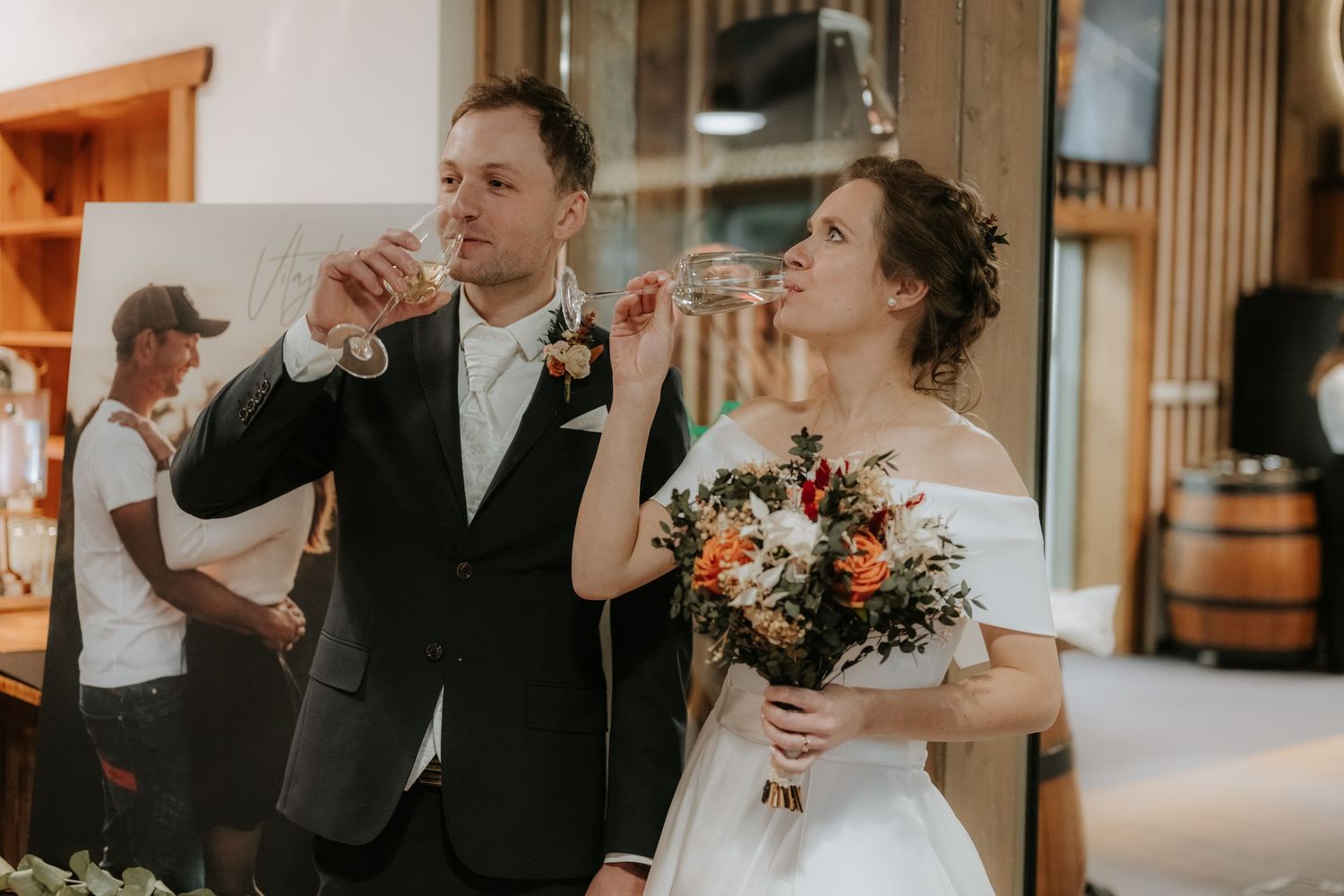 Bride holding bouquet and groom toasting with champagne glasses at elegant indoor wedding reception.