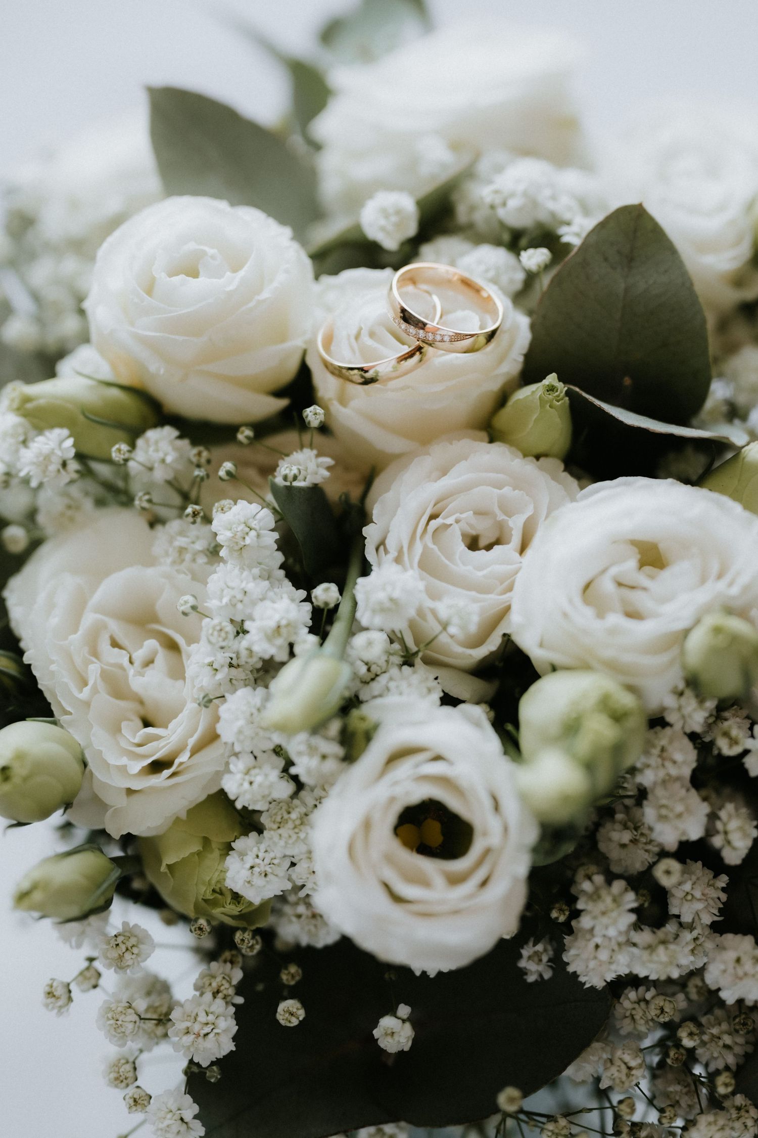 Elegant wedding bouquet of white roses and baby's breath with two gold wedding rings resting on top.