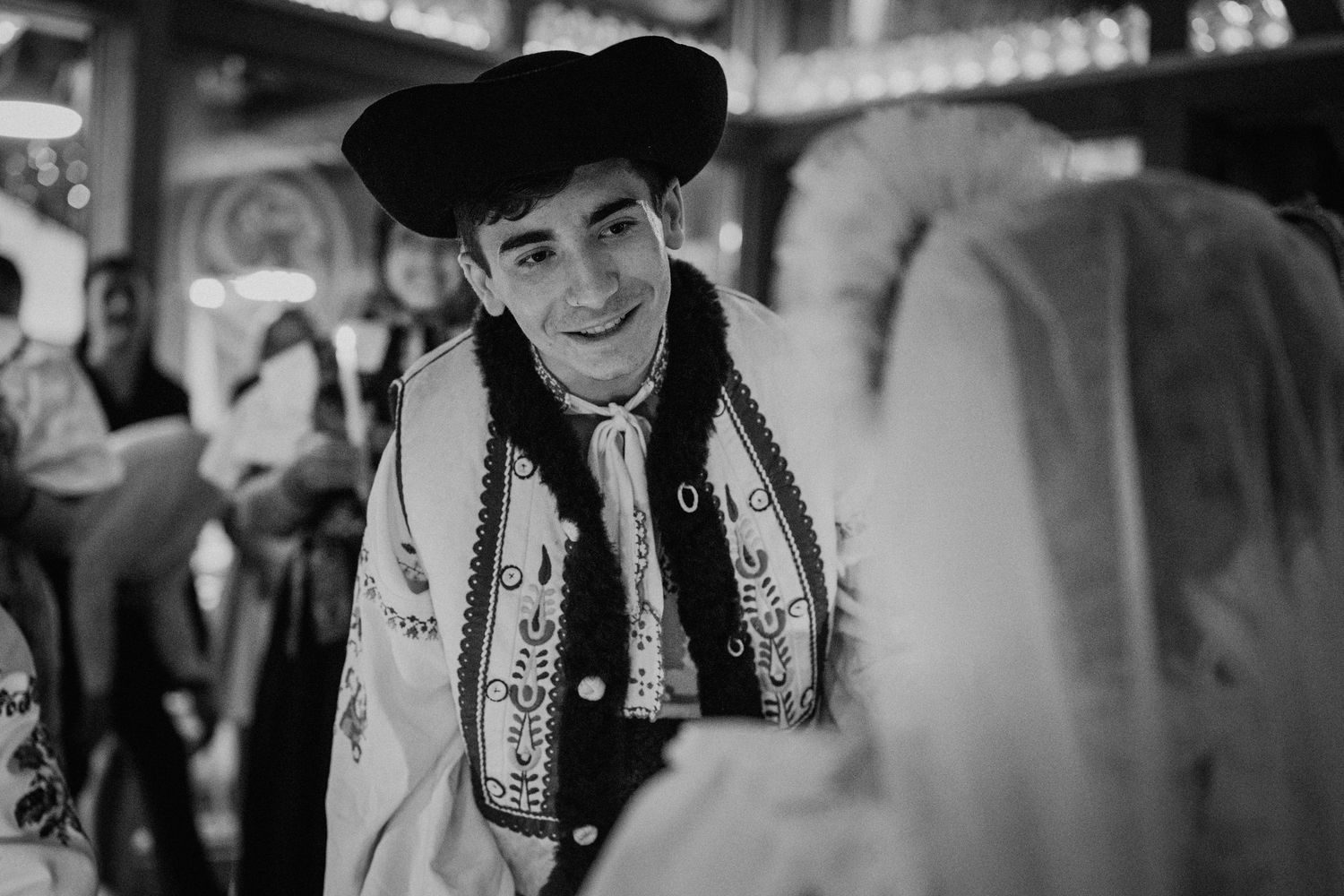 Young man in traditional folk costume smiling at a woman during a cultural dance event, black and white photo.