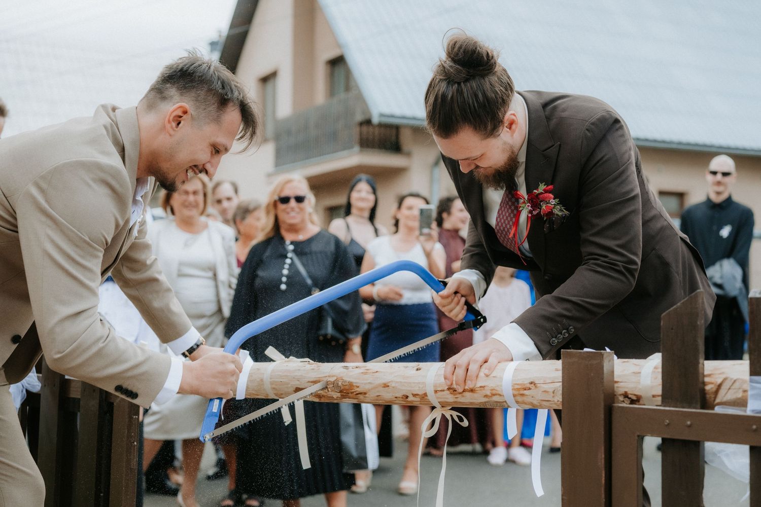 Two grooms sawing a log together at their wedding ceremony, a German tradition symbolizing teamwork in marriage.
