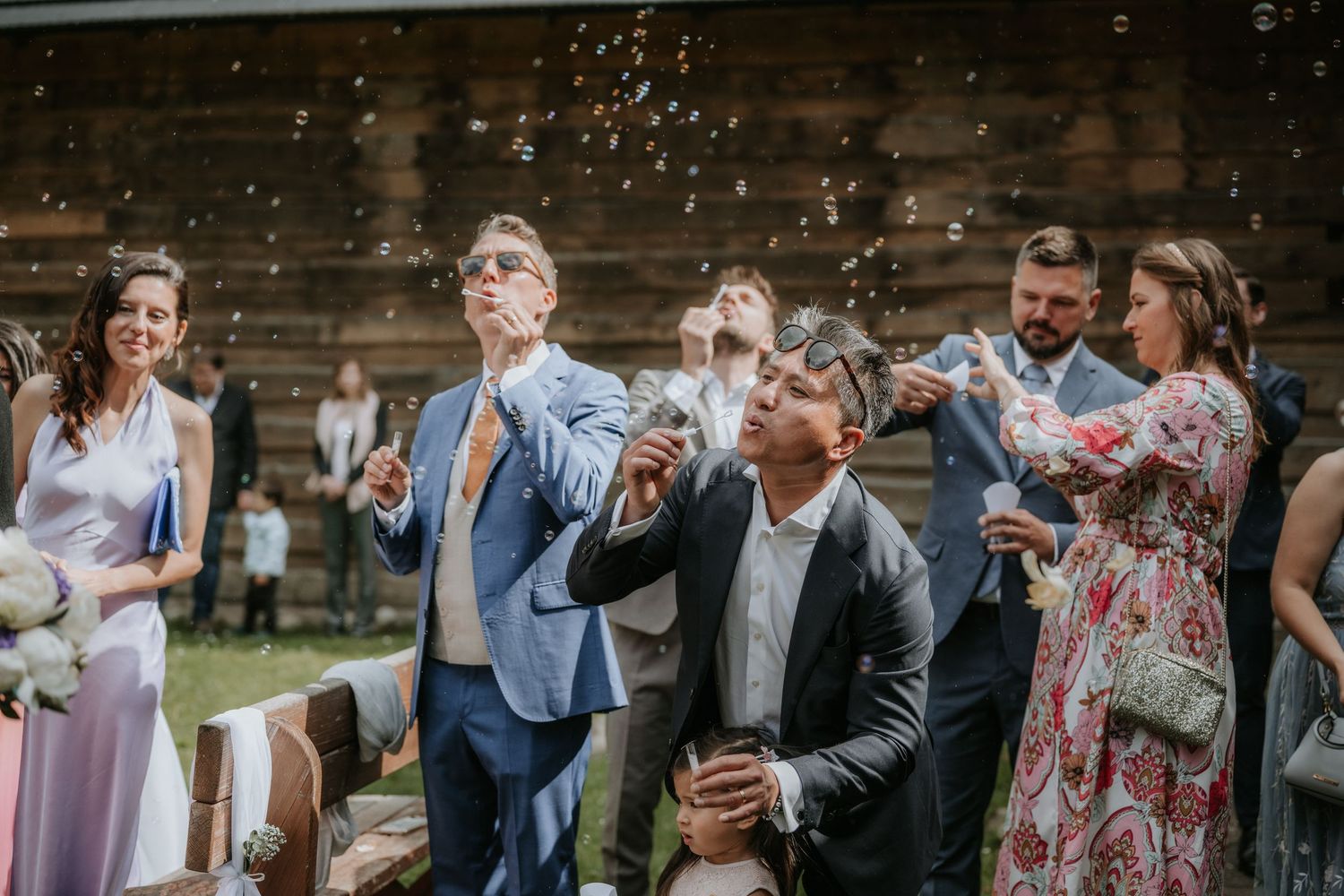 Wedding guests blowing bubbles outdoors at a rustic barn wedding celebration.