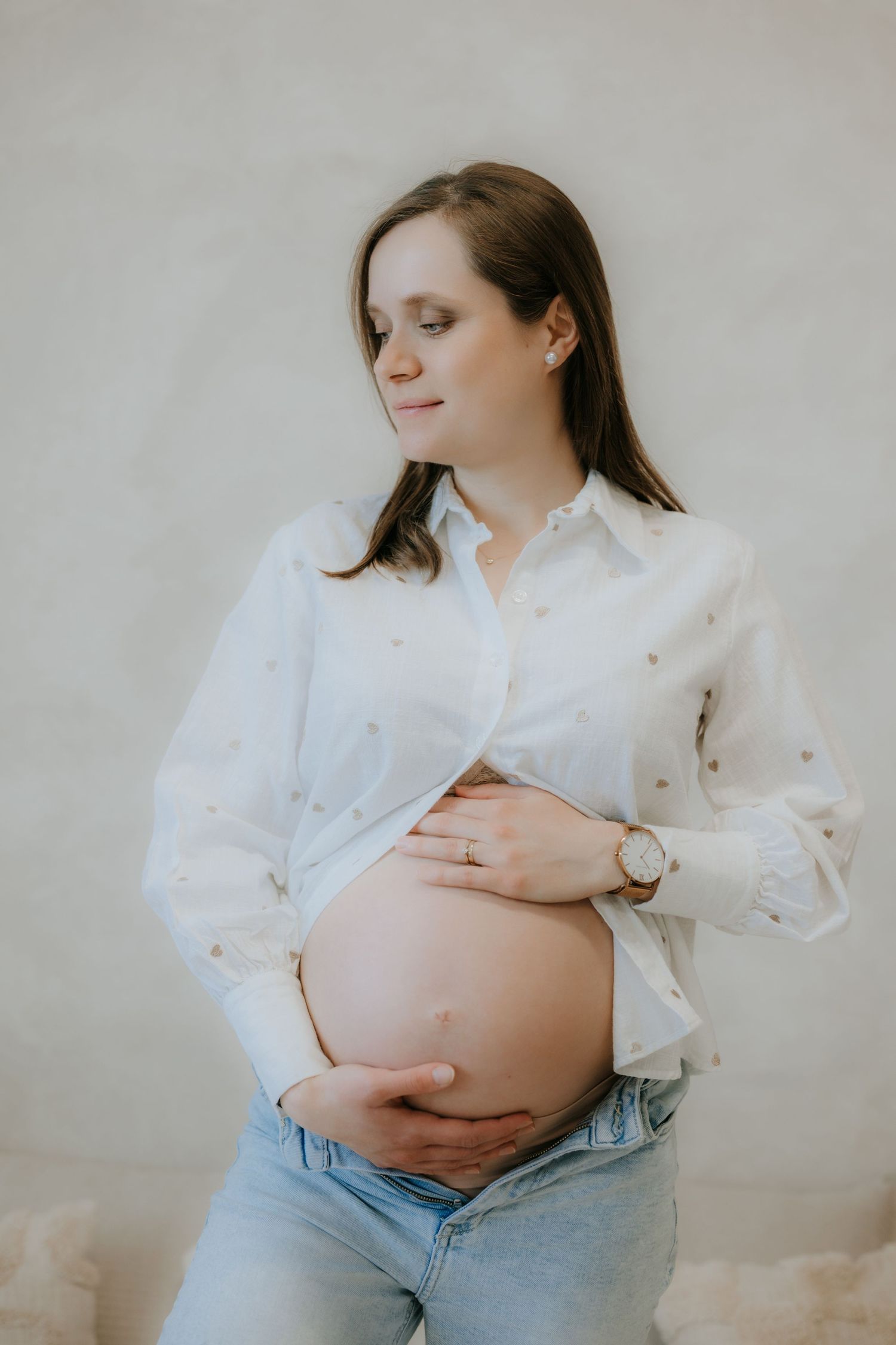 Serene pregnant woman in white shirt and jeans lovingly cradling her baby bump with eyes closed.