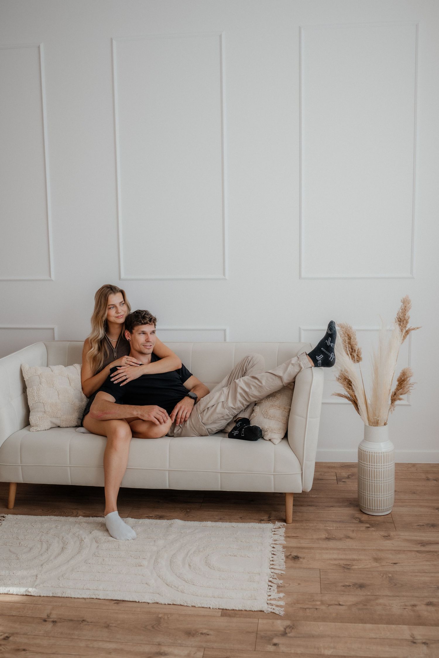 Relaxed couple cuddling together on a beige sofa in a bright minimalist living room.