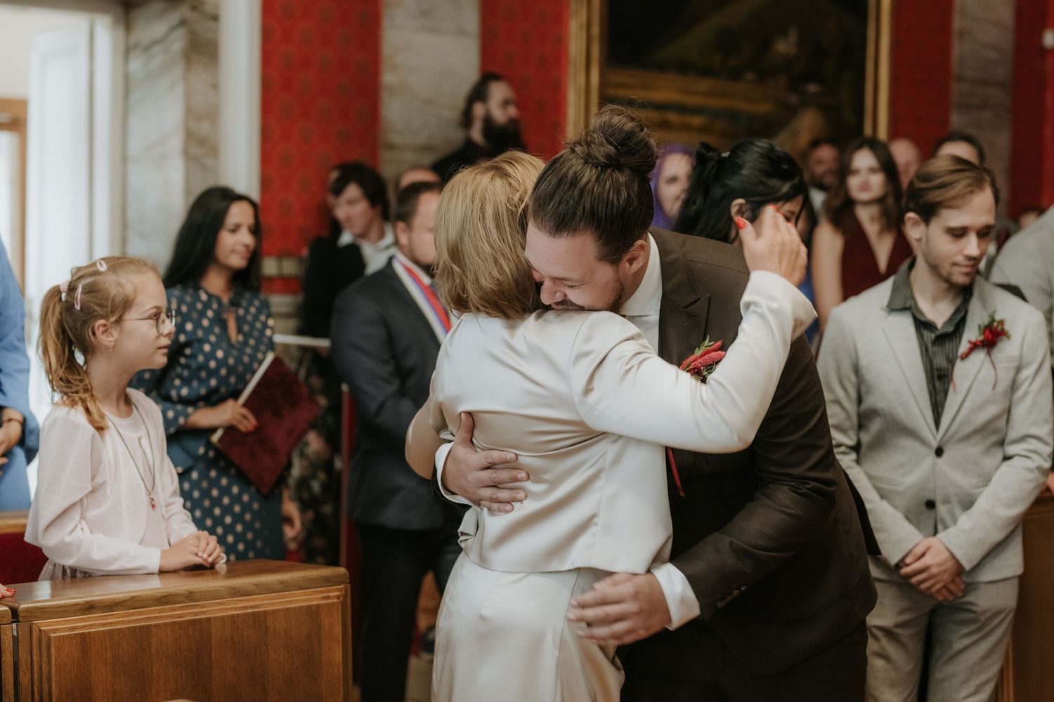 Emotional wedding ceremony hug between bride and guest in elegant venue with onlookers.