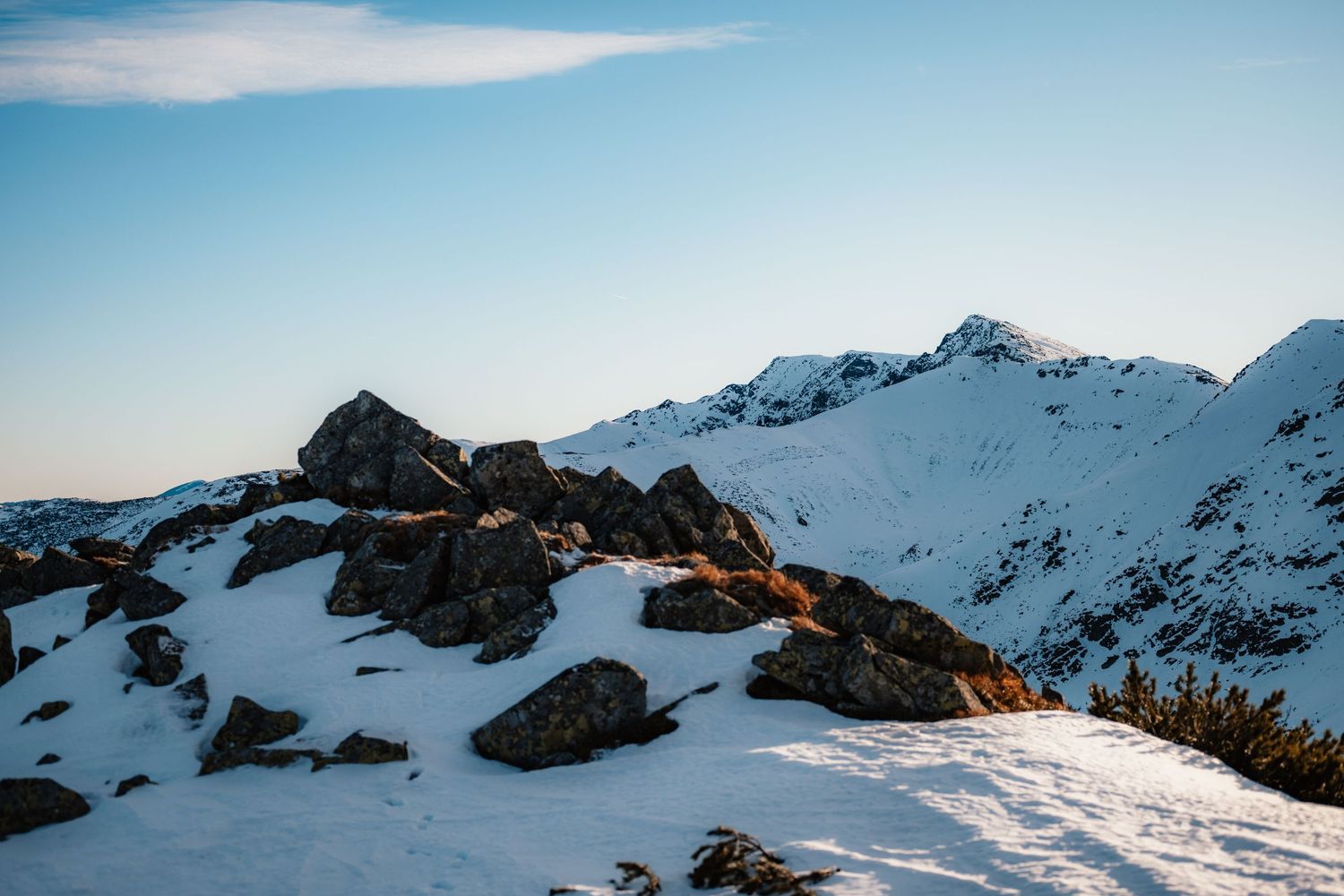 Snow-covered rocky mountain ridge with jagged peaks under clear blue winter sky.