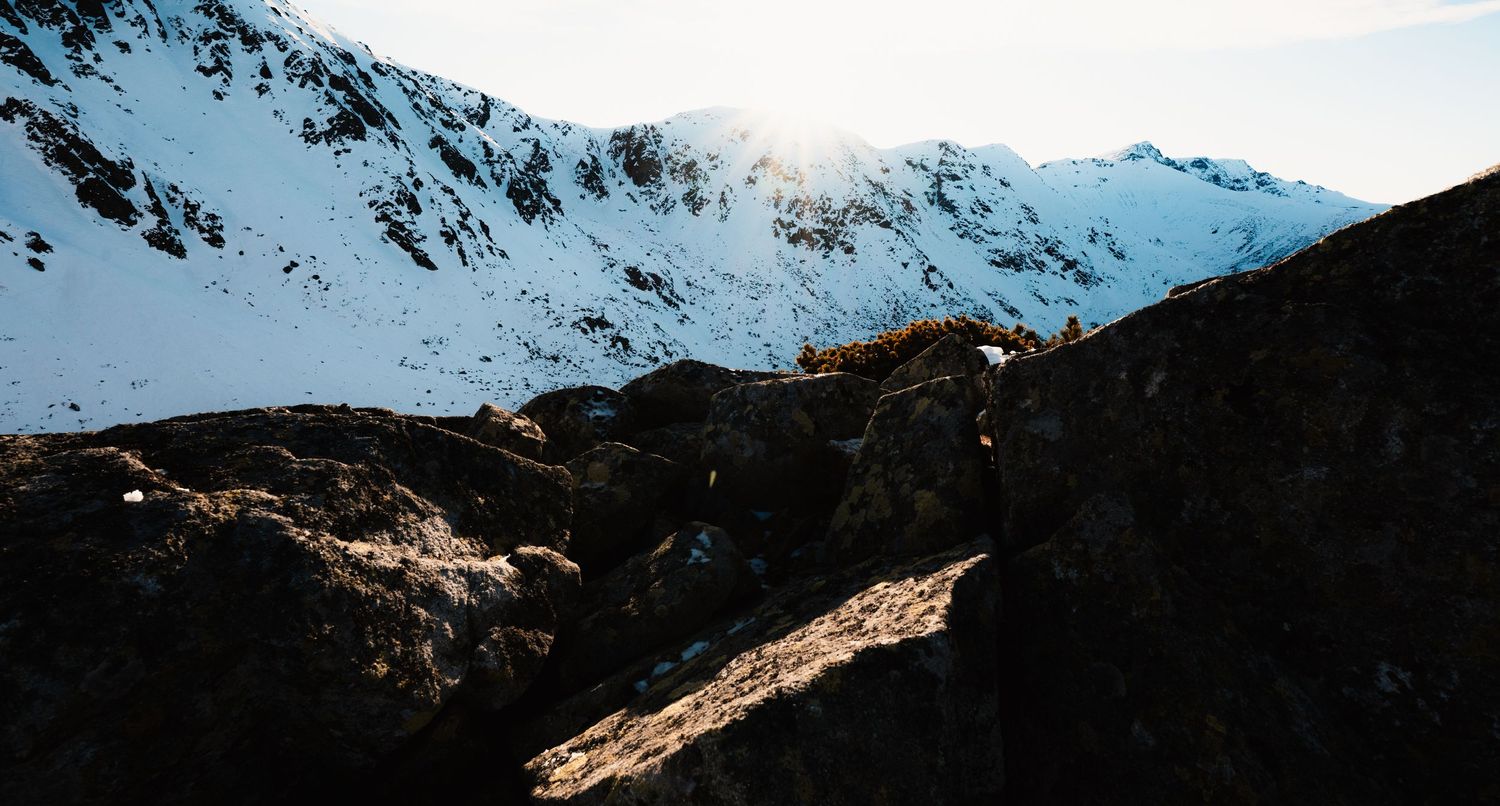Dark rocky terrain contrasting with bright snow-covered mountain peak under clear sky.