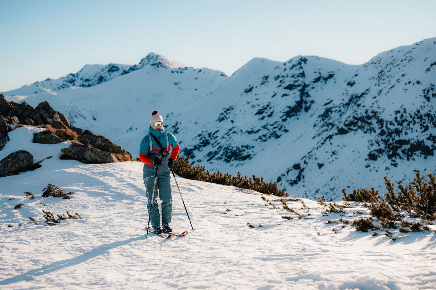 Solo skier with poles exploring a snowy mountain landscape on a clear winter day with rocky peaks behind.