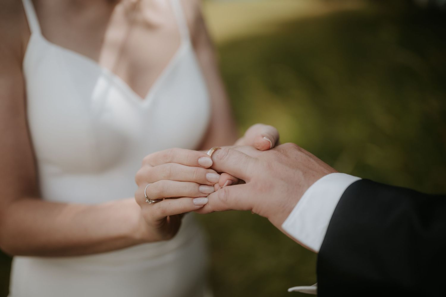 Bride placing a wedding ring on groom's finger during ceremony, close-up of hands in wedding attire.
