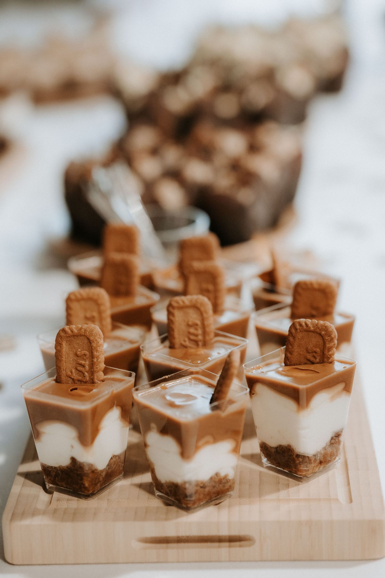 Elegant dessert cups with caramel, cream layers, and Biscoff cookies on a wooden board at an event.