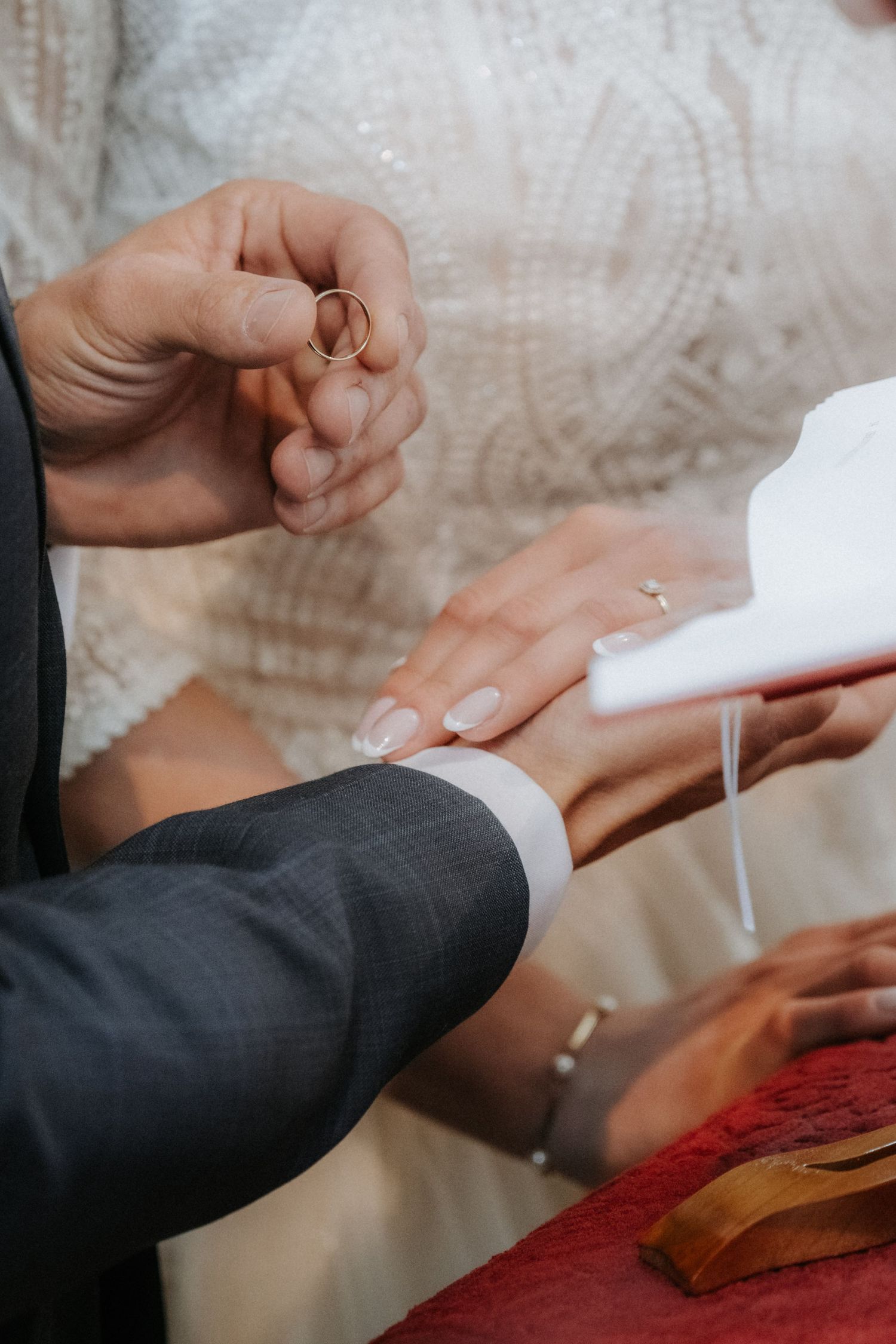 Bride placing a gold wedding ring on groom's finger during a wedding ceremony ring exchange.