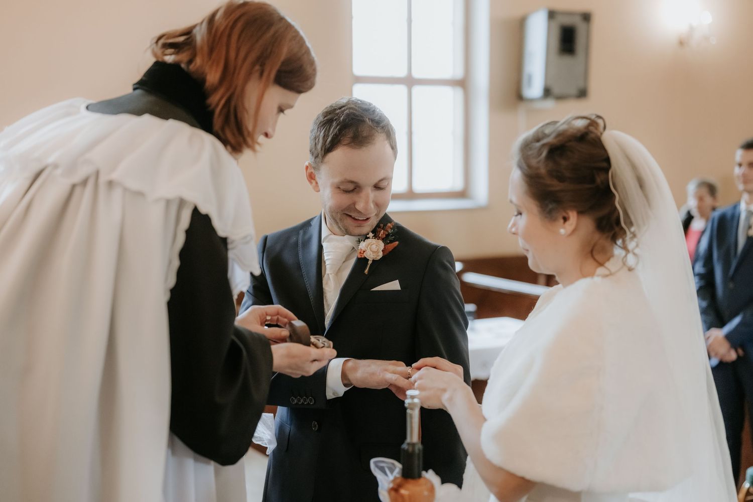 Bride and groom exchanging wedding rings with officiant during a church ceremony.