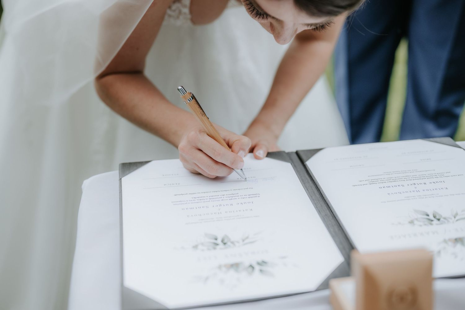 Bride signing wedding certificate documents with gold pen during marriage ceremony.