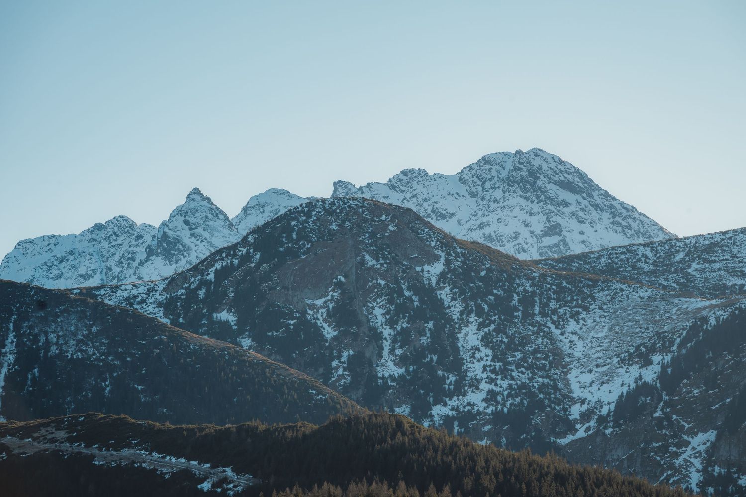 Rugged snow-covered Tatra mountain peaks with rocky ridges under pale blue winter sky.