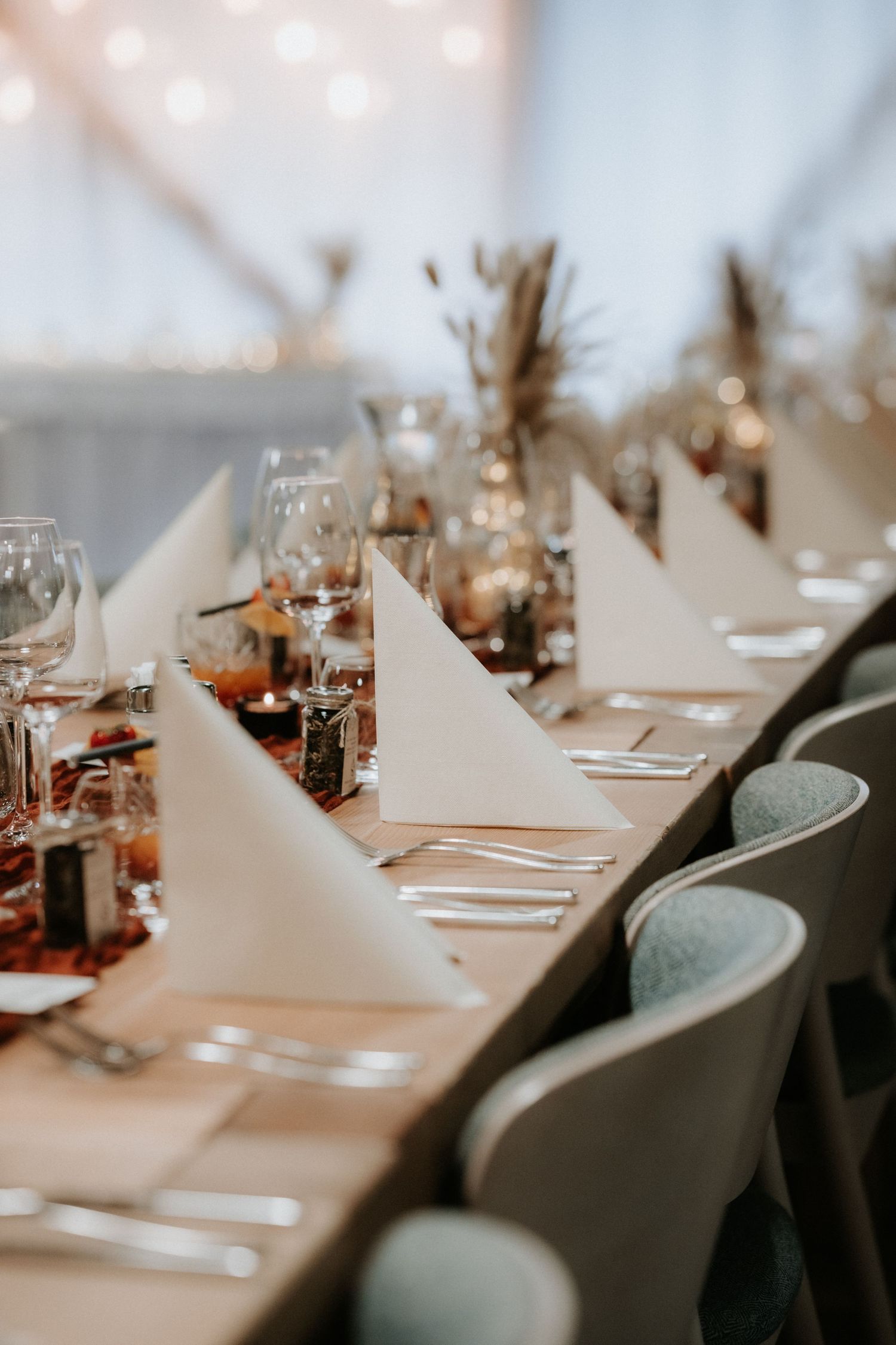 Elegant wedding reception table set with white folded napkins, wine glasses, and sage green chairs.