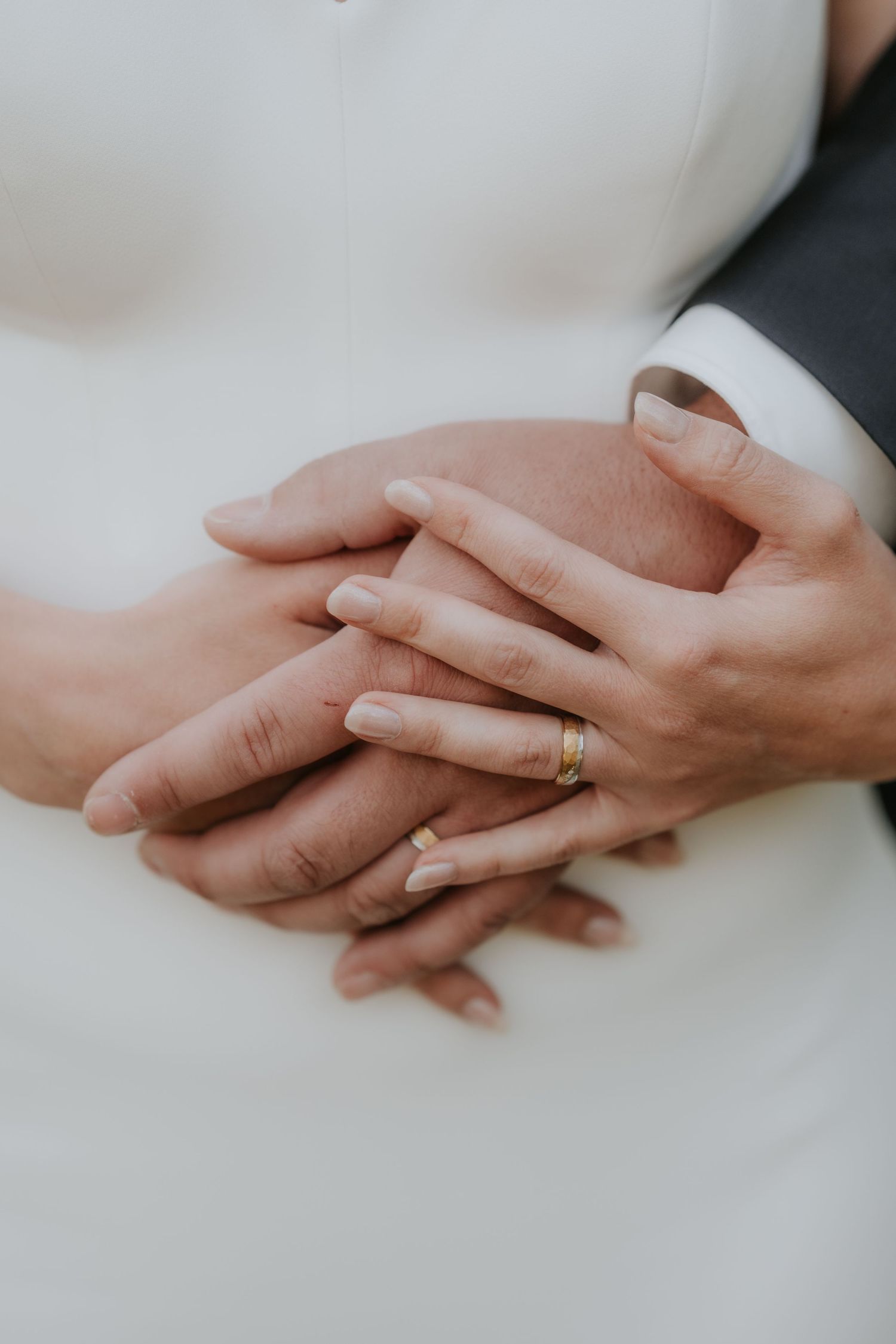 Close-up of newlywed couple holding hands, showcasing a gold wedding ring on the bride's finger.