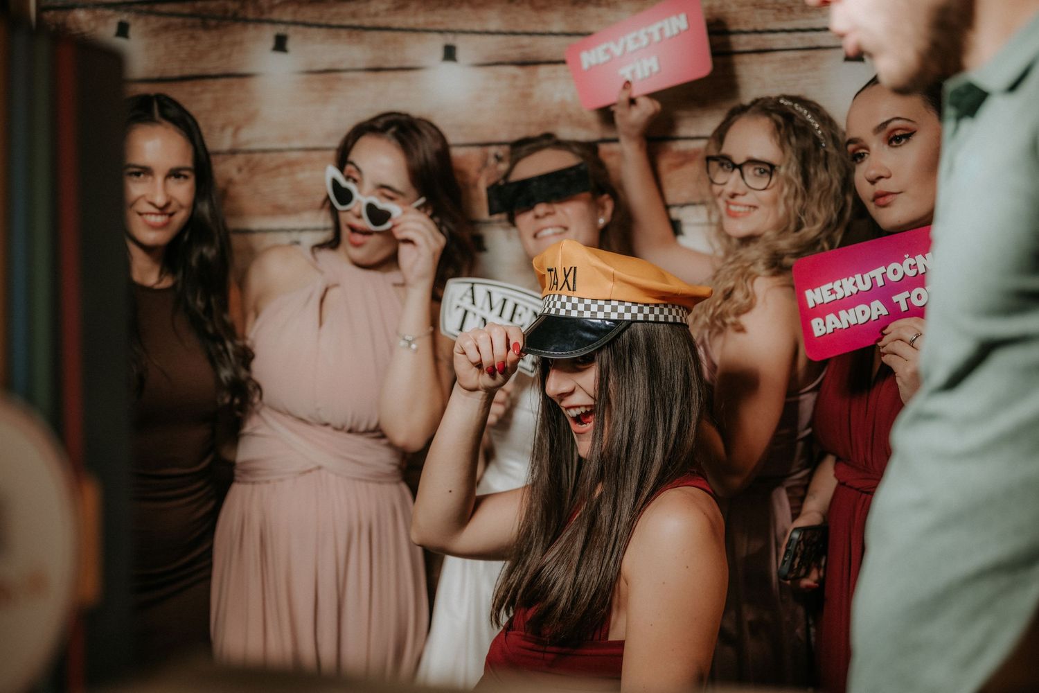 Group of women celebrating at a party, posing with fun props including sunglasses and colorful signs.