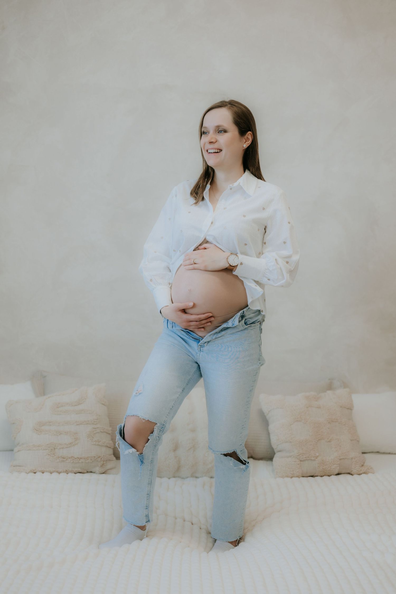 Glowing pregnant woman in white shirt and ripped jeans cradles her bare baby bump.