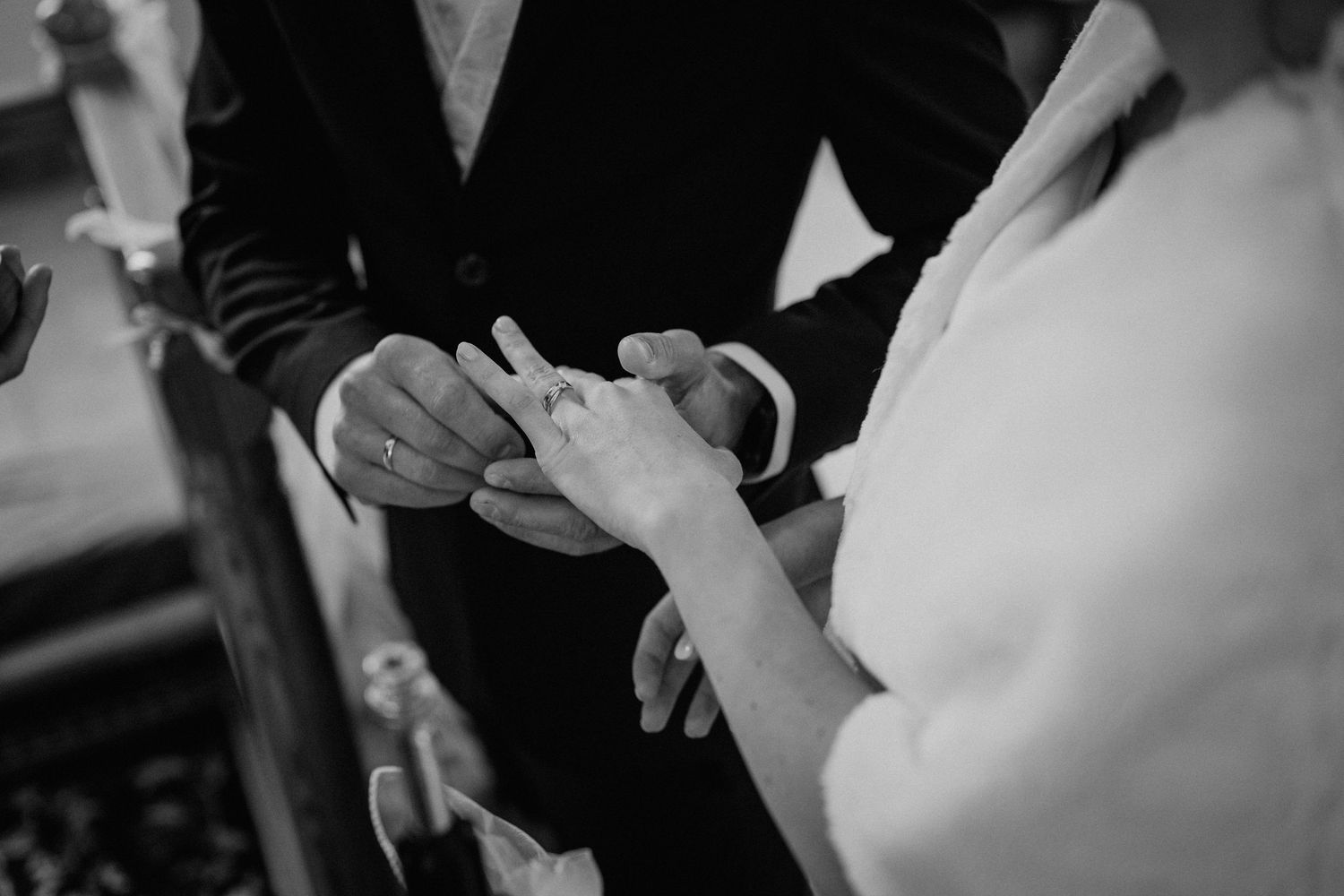 Groom placing wedding ring on bride's finger during ceremony in black and white photo.