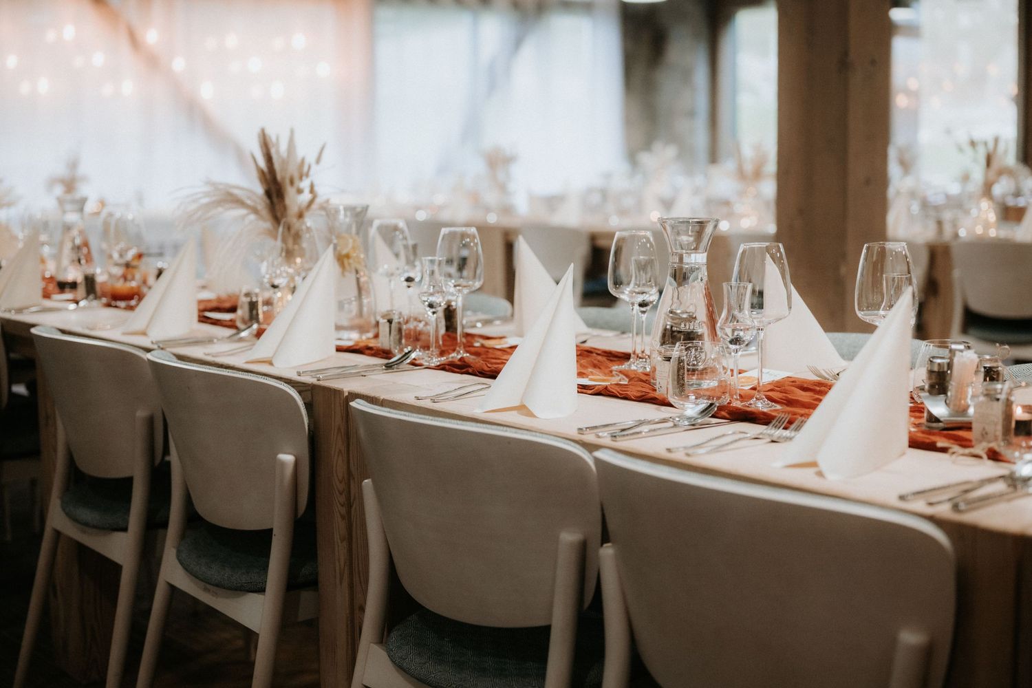 Elegant wedding reception table set with white napkins, crystal glasses, and terracotta runners in a warmly lit venue.