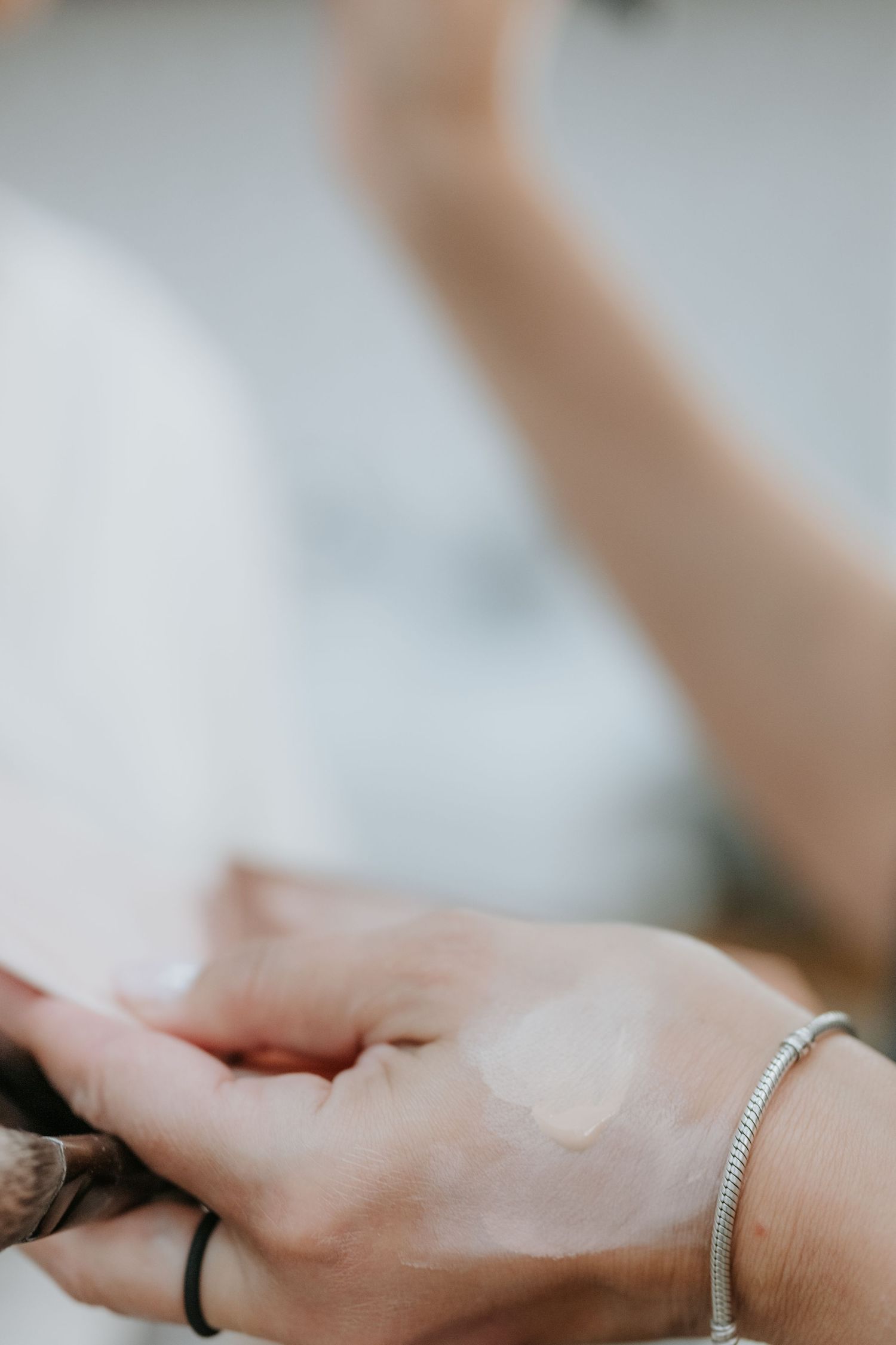 Close-up of hands applying foundation makeup with a silver bracelet and black ring visible.