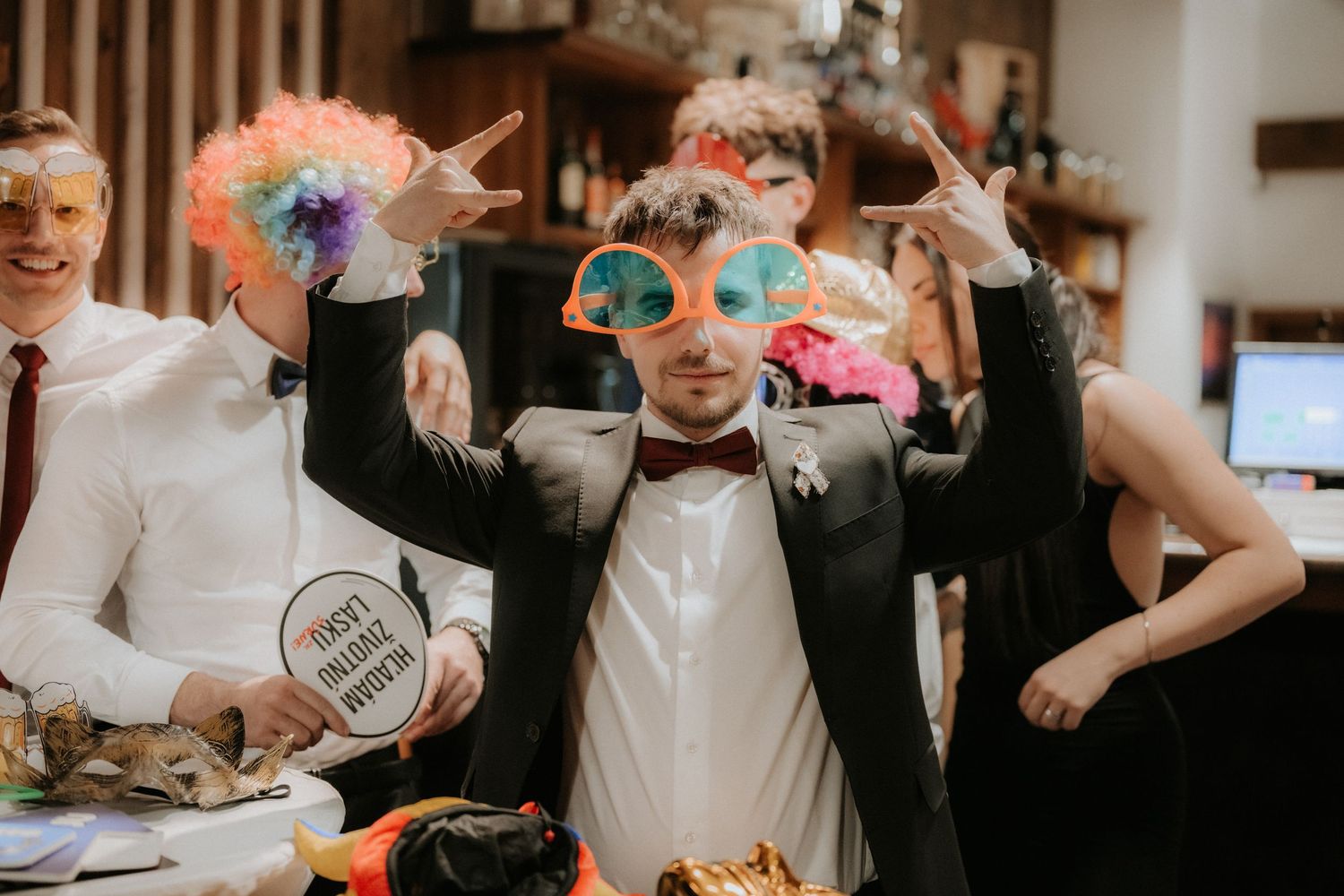 People posing with fun photo booth props at a party, wearing colorful wigs and novelty glasses.