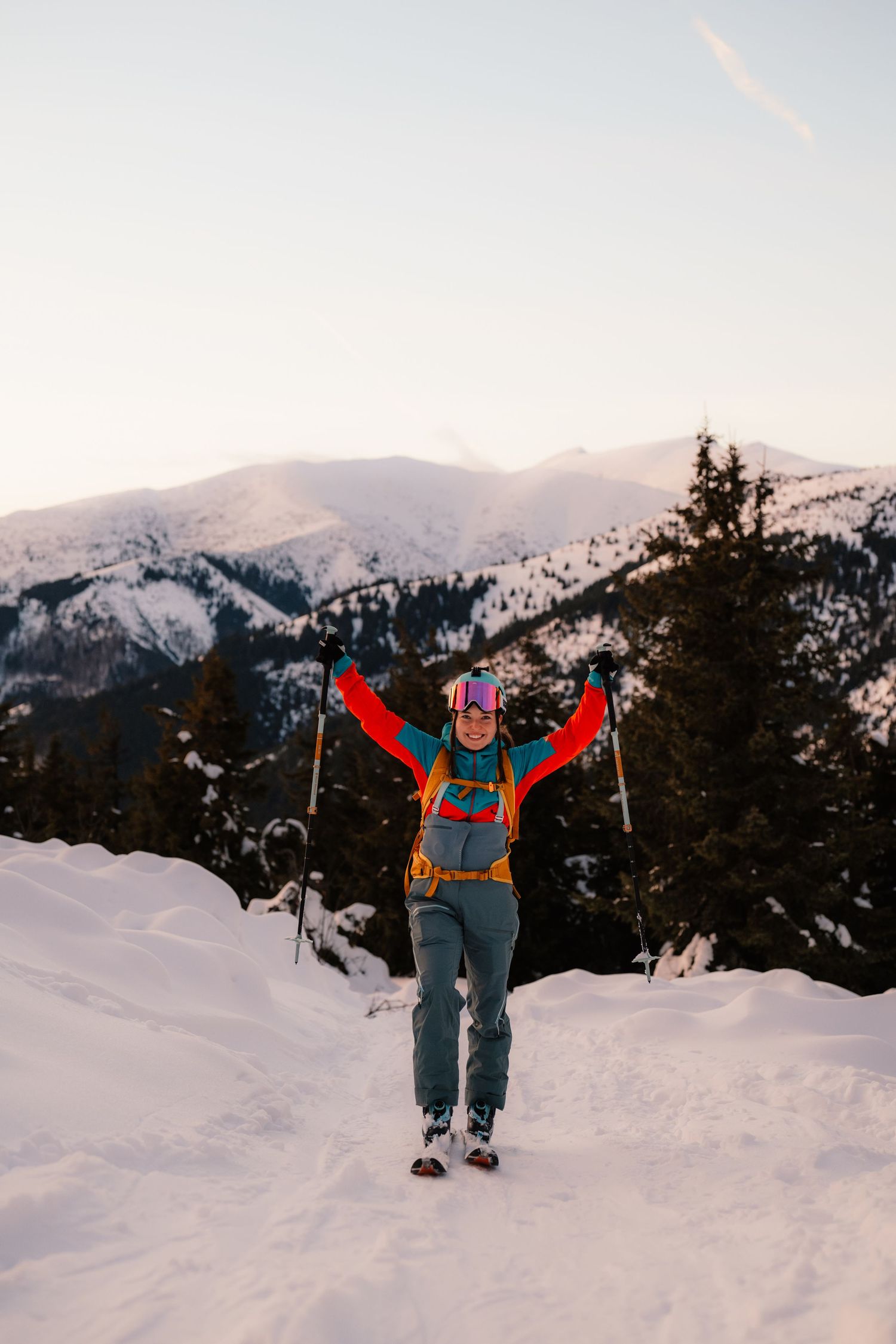 Excited female skier raising arms in triumph on snowy mountain with peaks in background.