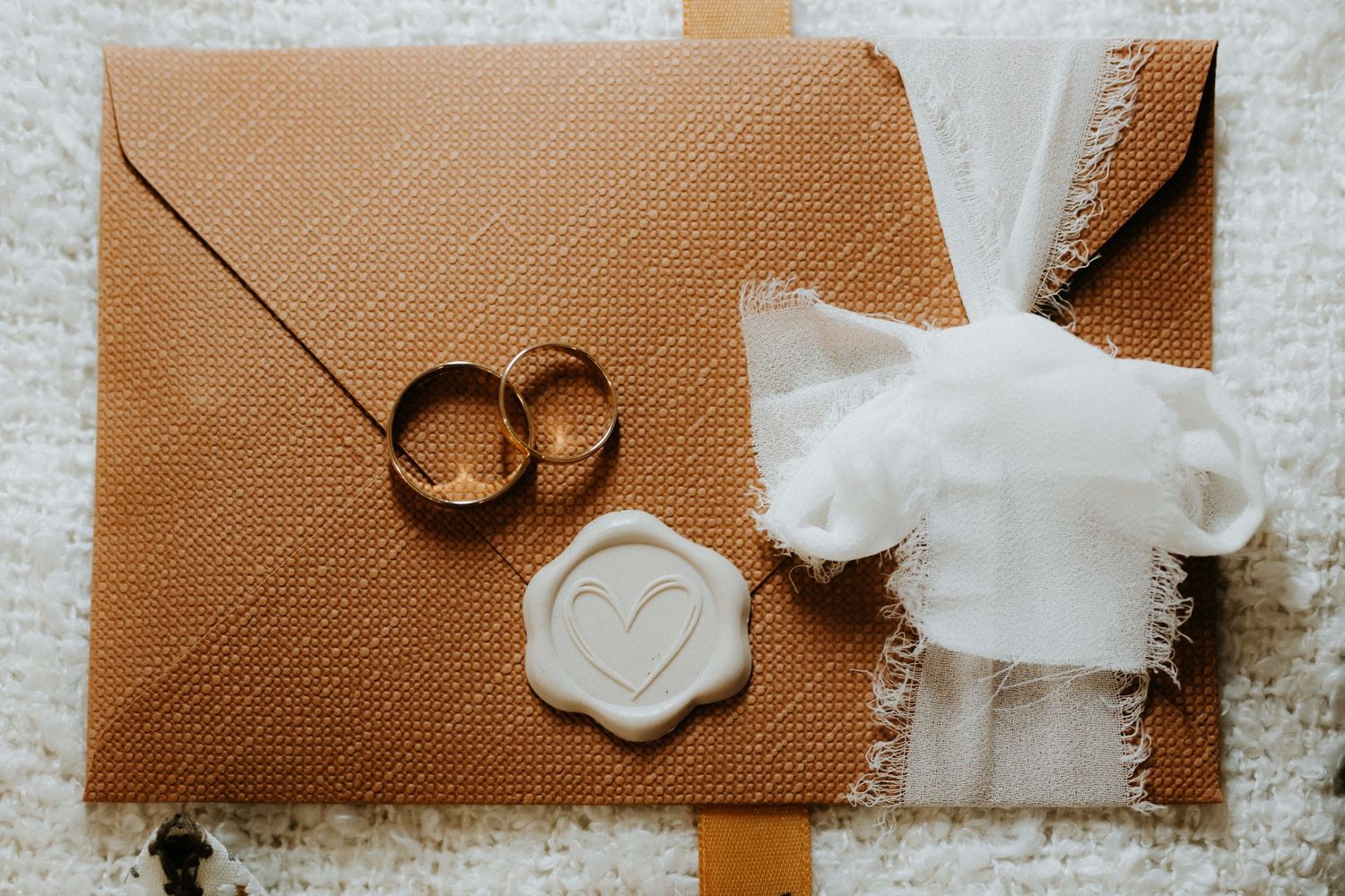 Two gold wedding rings on a brown wax-sealed envelope with white fabric ribbon accent.