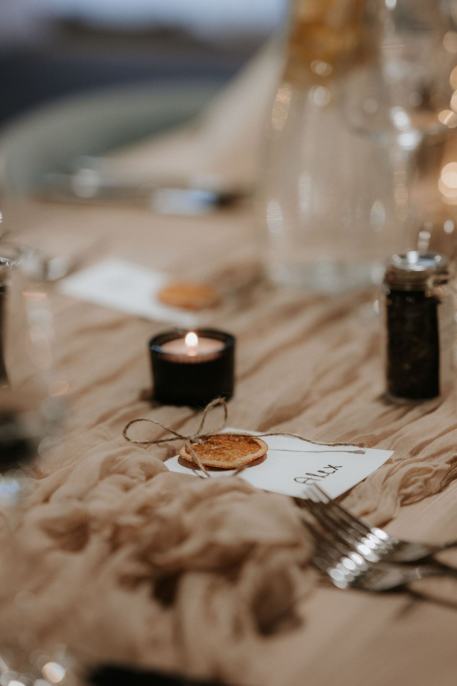 Rustic wedding table setting with wax seal place cards, black tealight candle, silverware, and soft linen runner.