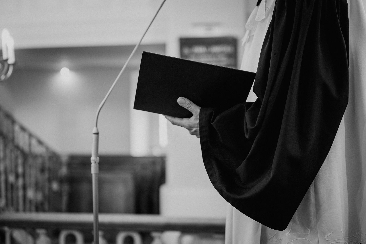 Black and white photo of a priest in robes holding a book at a church podium.