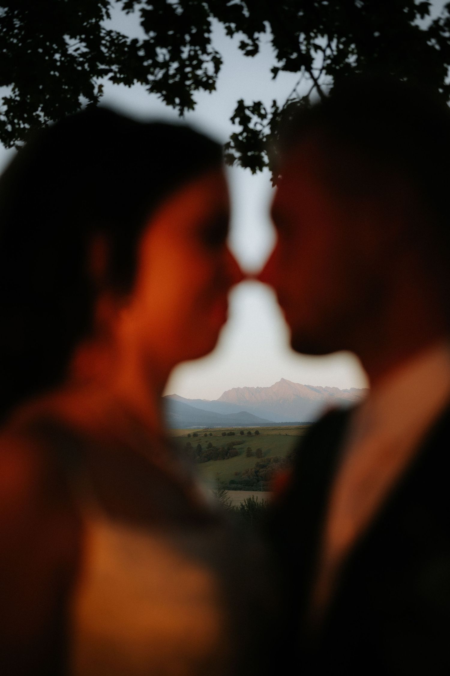 Romantic silhouette of couple almost kissing with mountain landscape visible between them at golden hour.