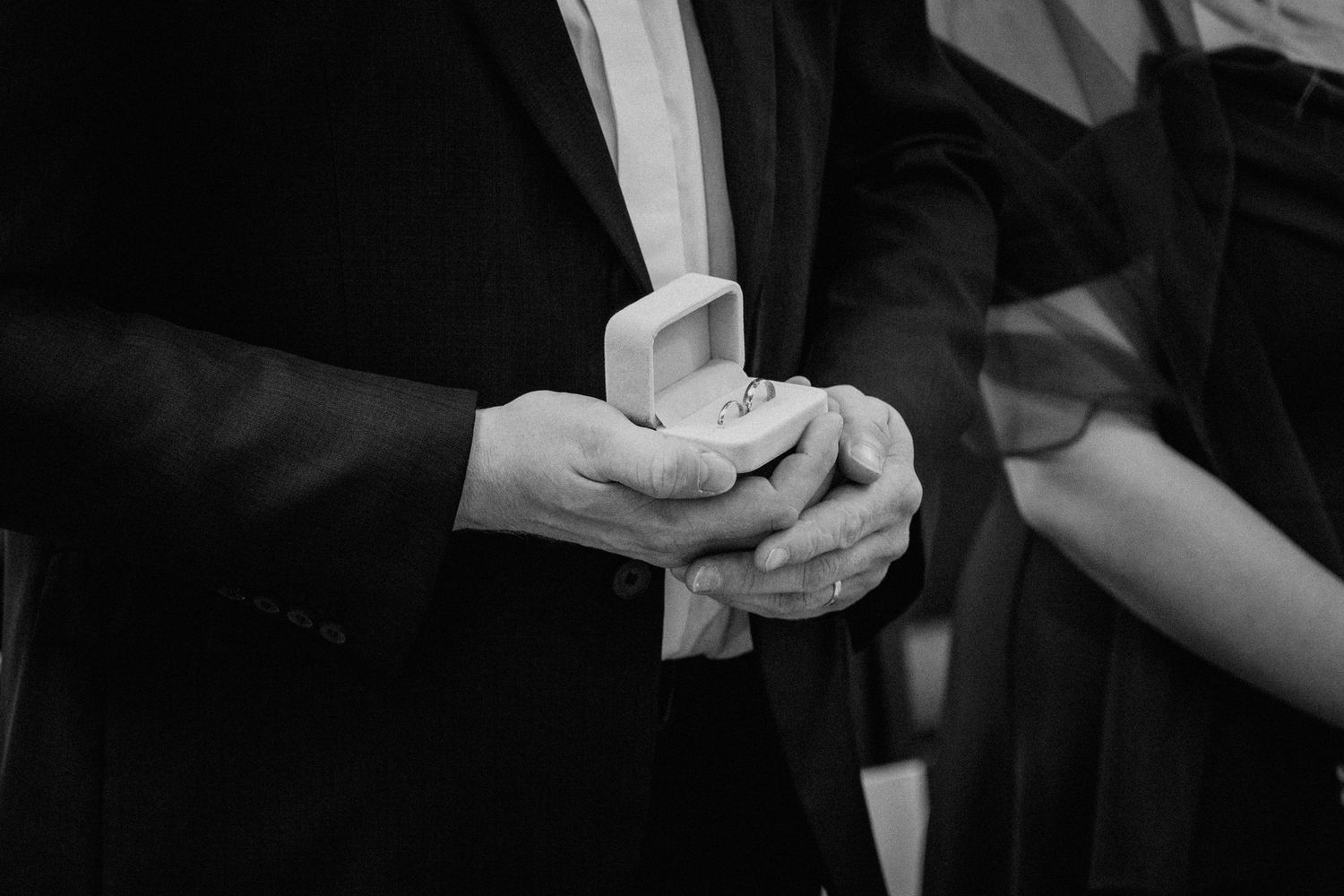 Black and white photo of hands holding a wedding ring box during a marriage ceremony.