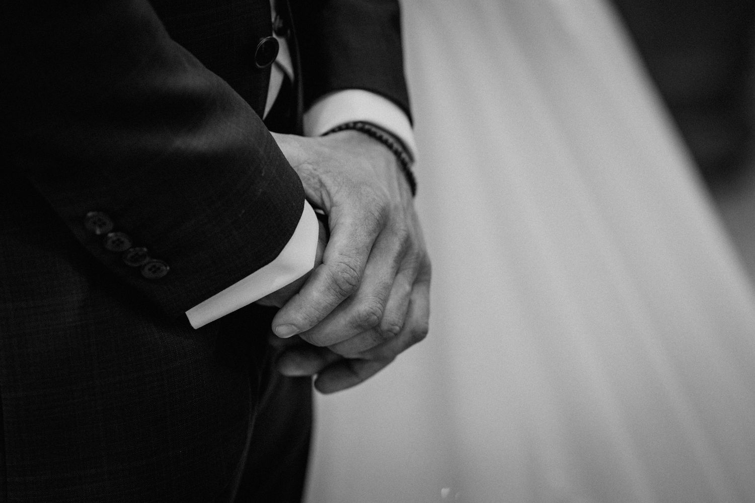 Black and white photo of groom clasping hands in a suit at a wedding ceremony.
