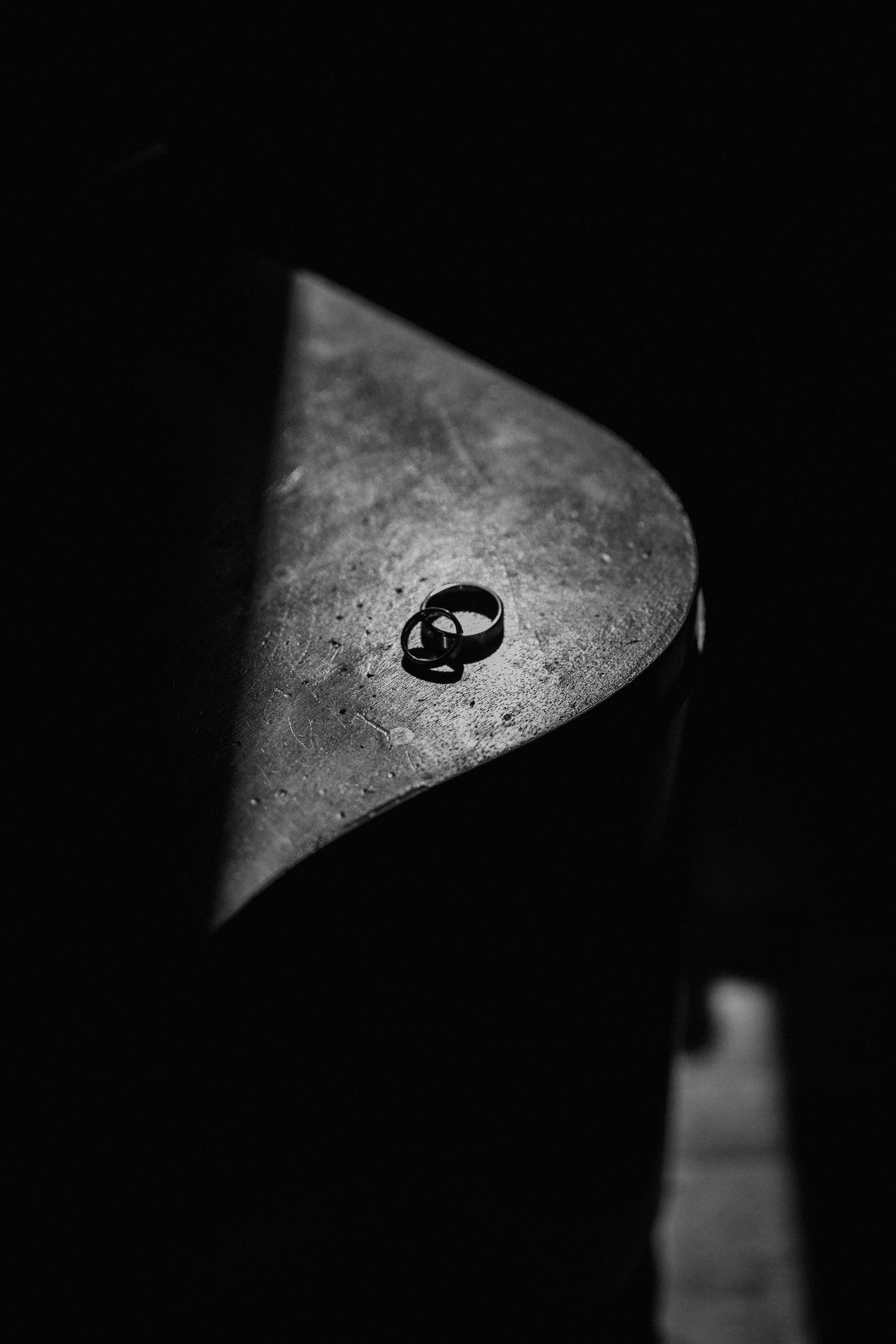 Black and white photo of two wedding rings resting on a dark surface, dramatically lit from above.