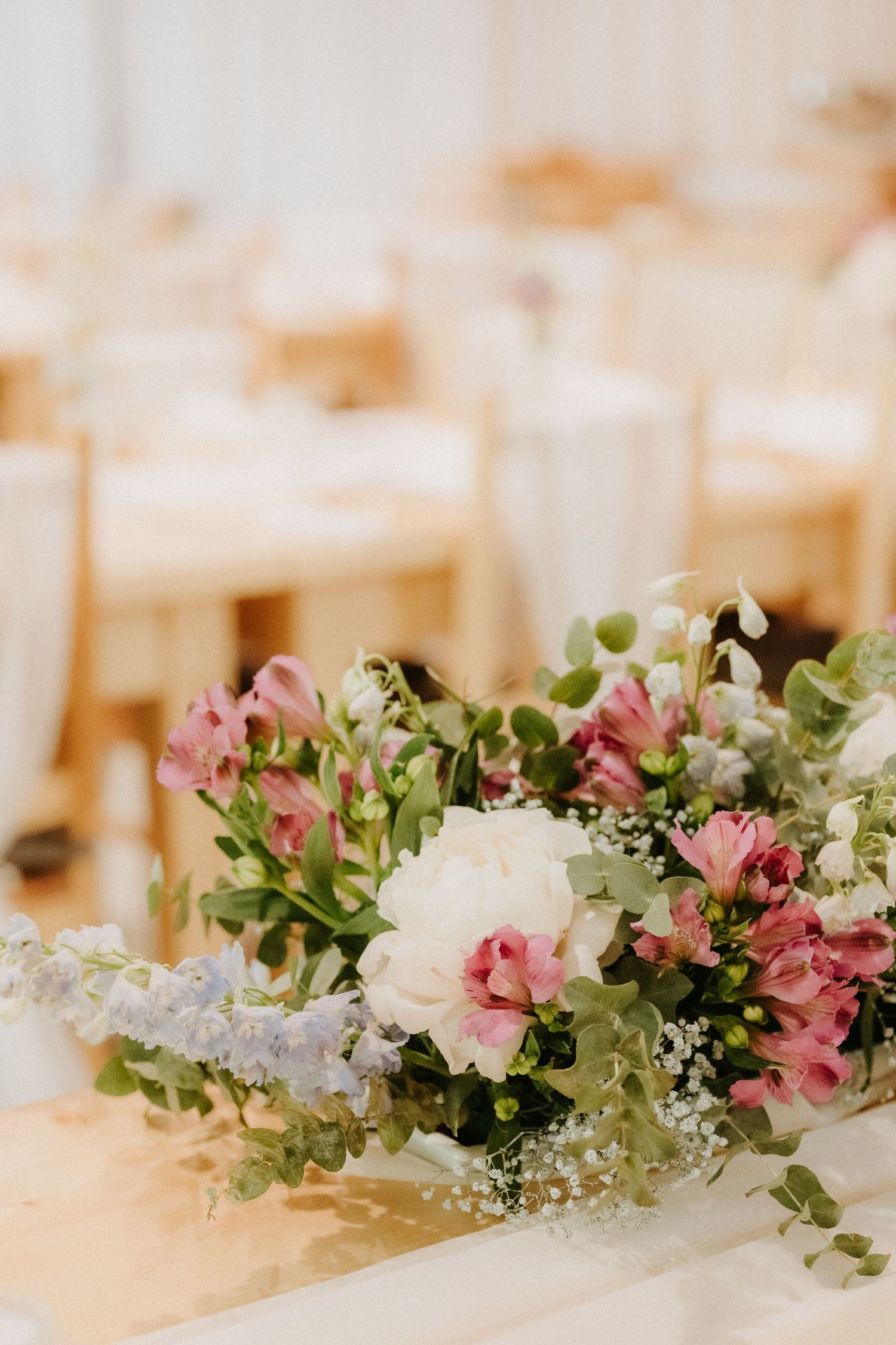 Elegant wedding reception bouquet with pink alstroemeria, white peonies, and greenery on a gold table.