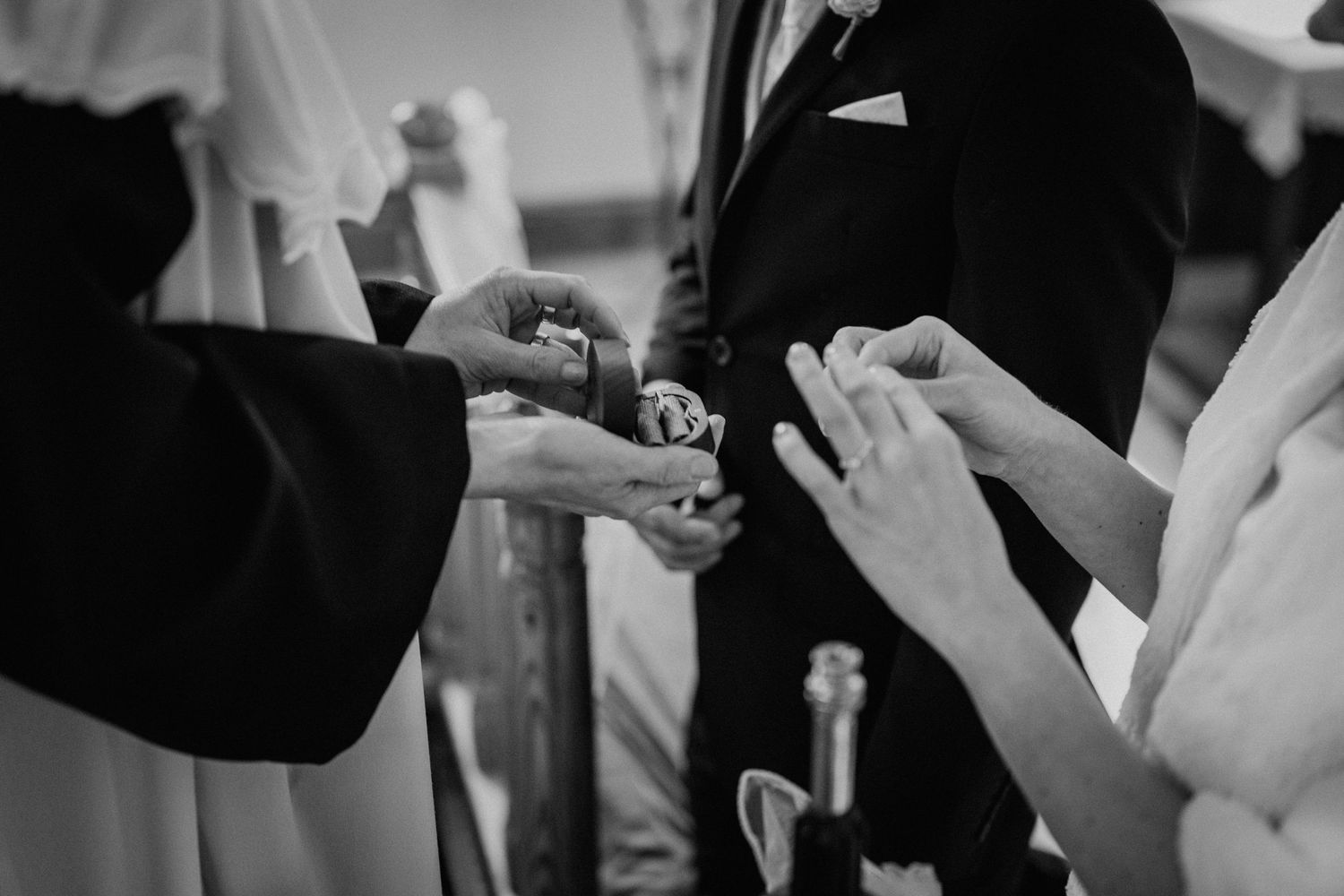 Black and white wedding ring exchange ceremony, bride and groom hands with officiant holding rings.