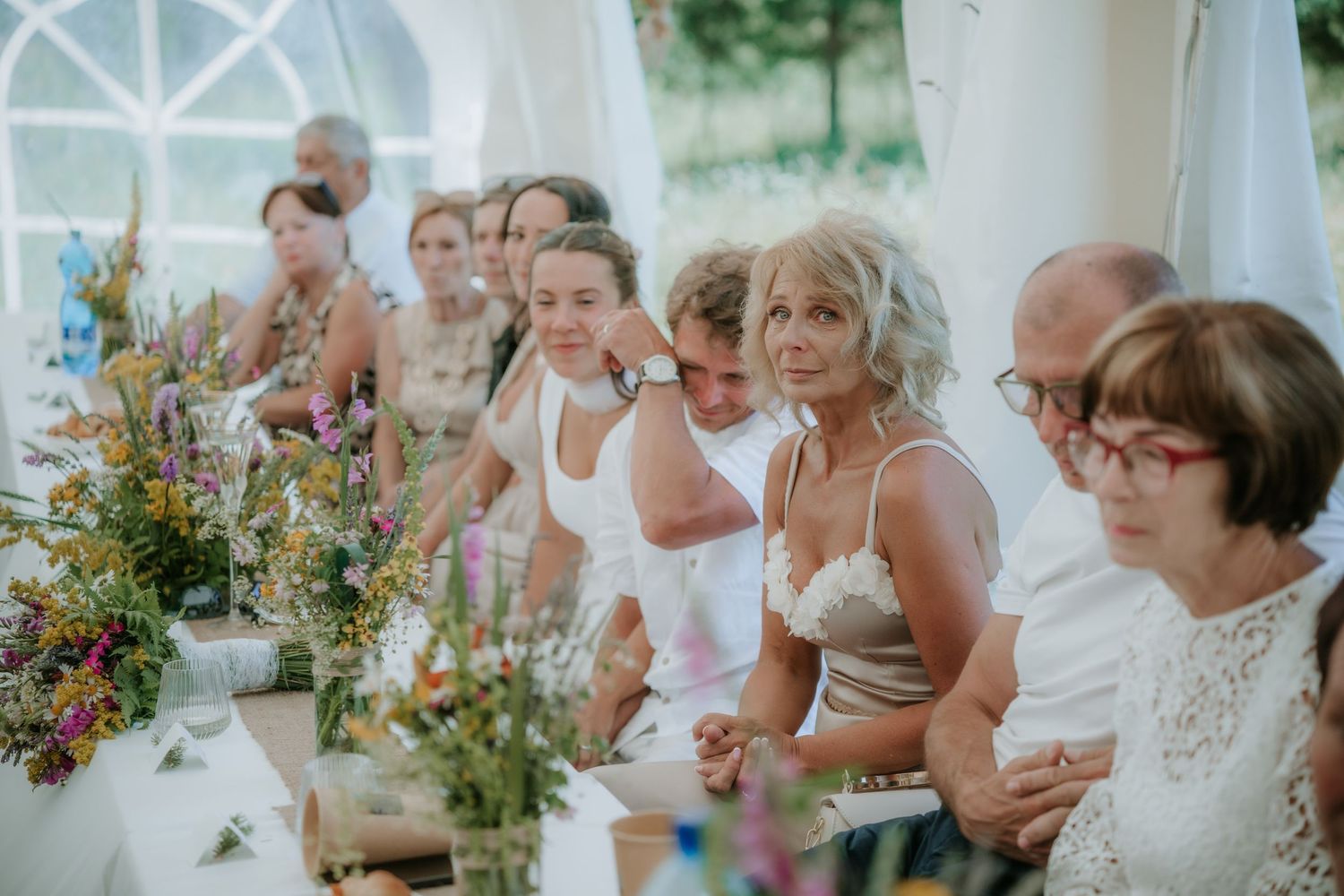 Guests seated at a floral-decorated wedding reception table inside a marquee, enjoying the celebration.